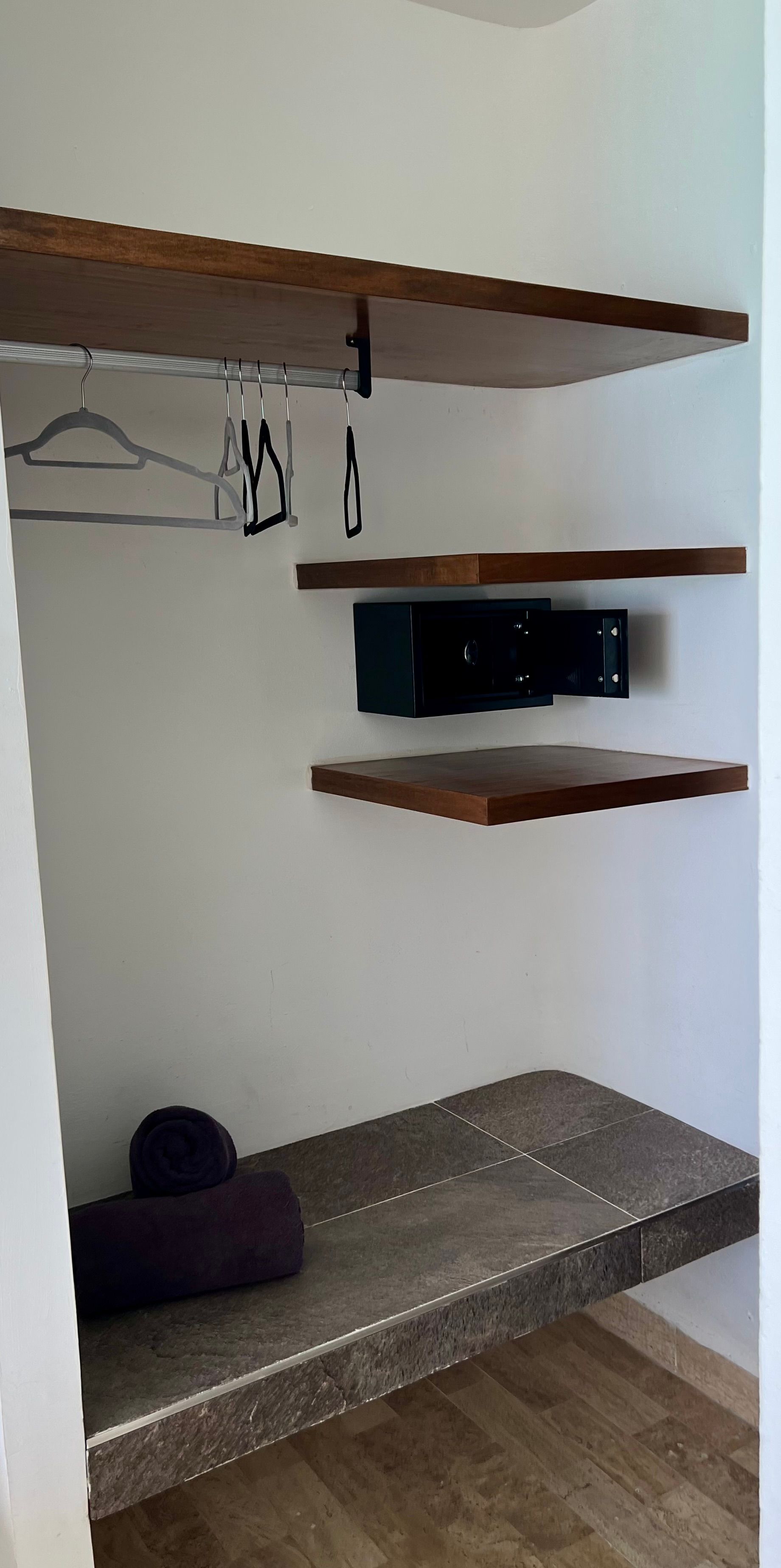 Armario con estantes de madera, caja fuerte, perchas y banco con toalla.