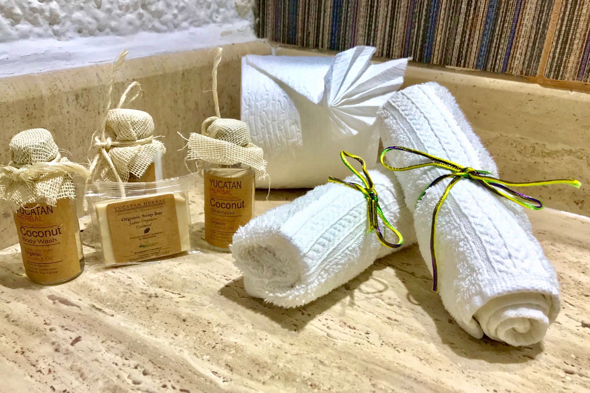Artículos de aseo del spa: toallas blancas enrolladas, botellas pequeñas, jabón envuelto, sobre una superficie de mármol.