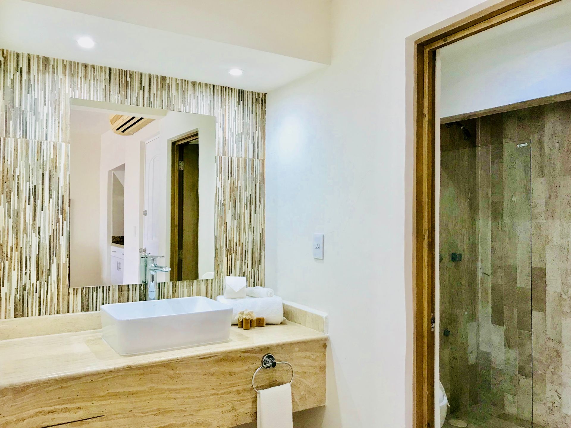 Baño moderno con pared de piedra, lavabo, espejo y ducha de cristal.