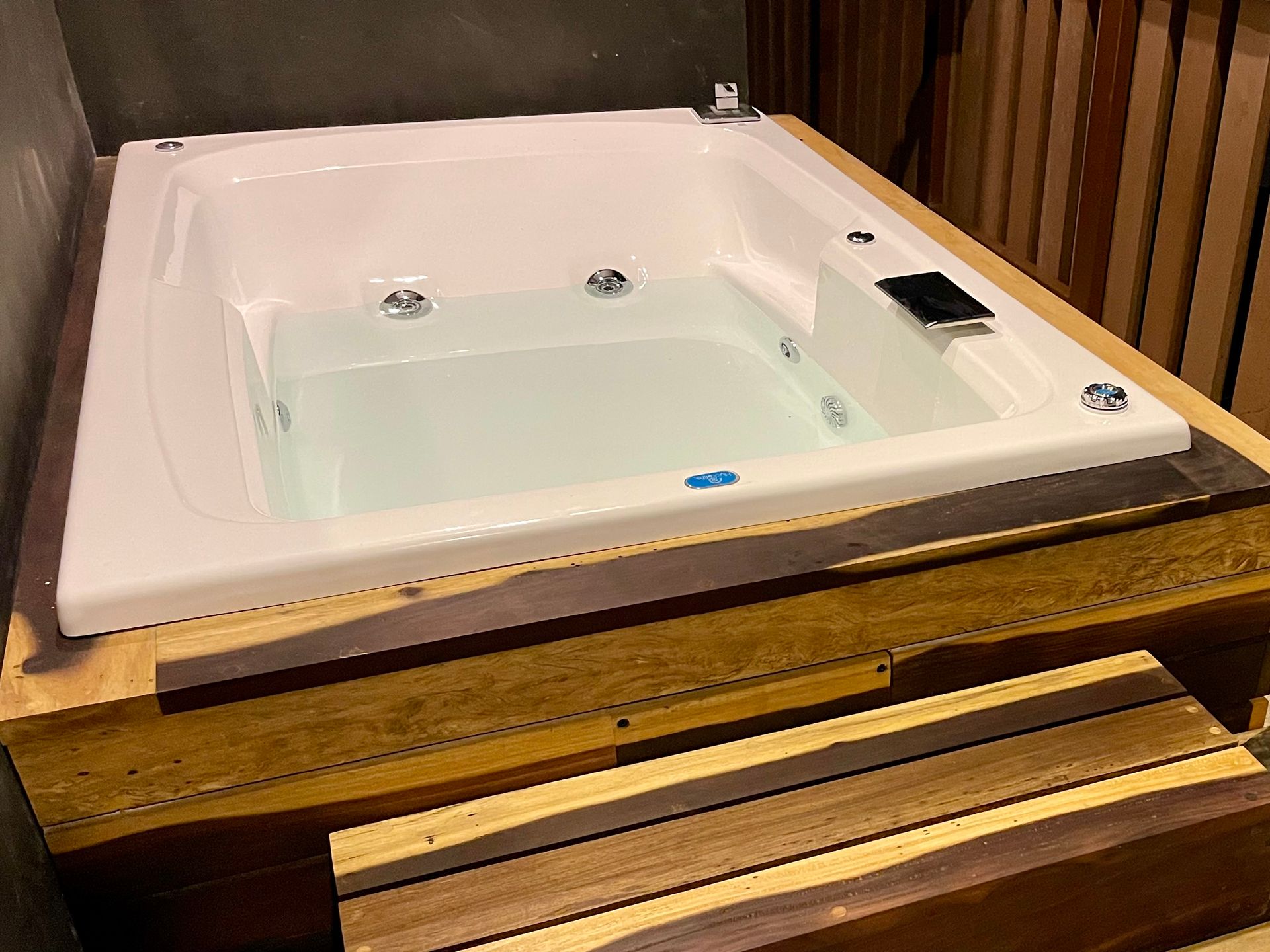 Bañera de hidromasaje rectangular de color blanco llena de agua sobre una base de madera.