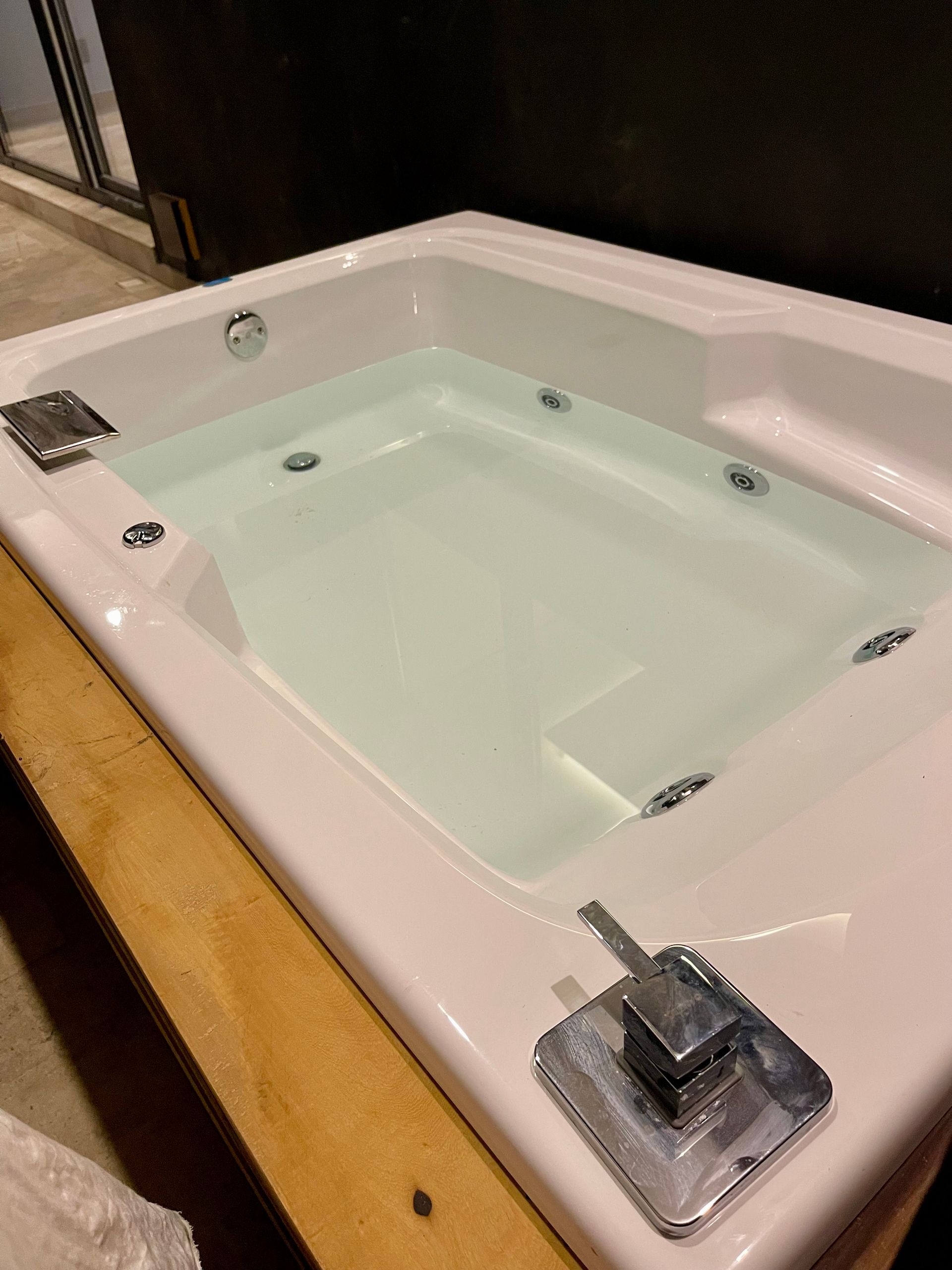 Bañera de hidromasaje rectangular de color blanco llena de agua, con chorros y accesorios cromados visibles.
