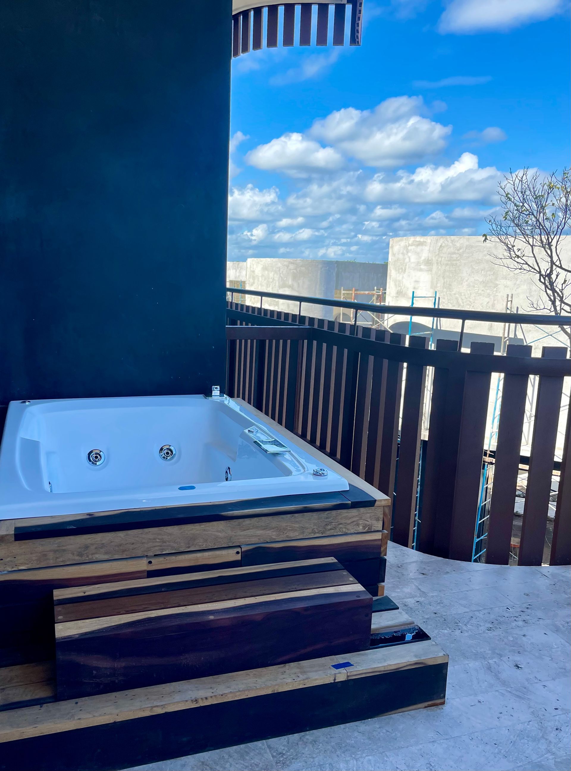 Jacuzzi al aire libre sobre una terraza de madera, con cielo azul y nubes de fondo.