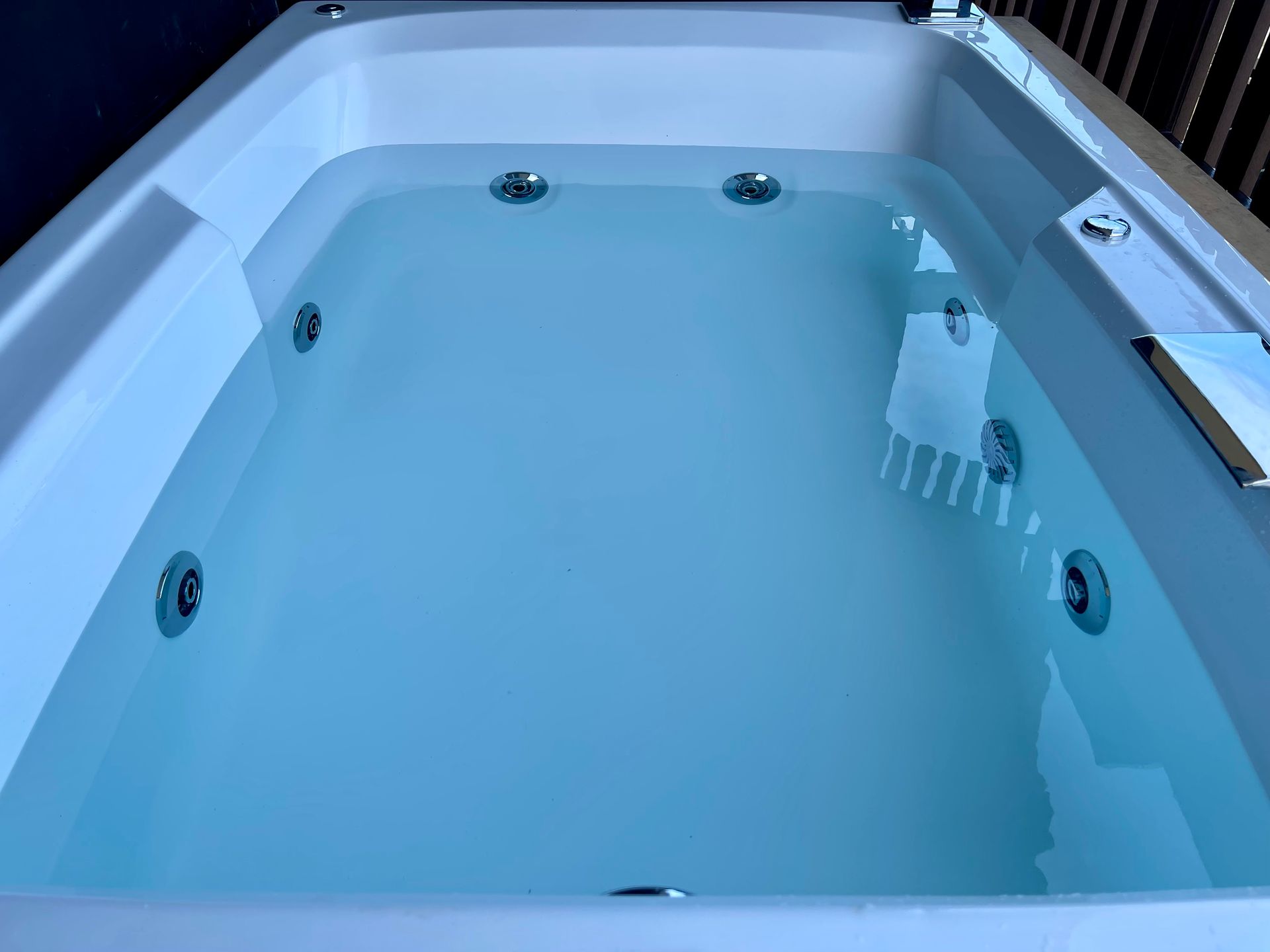 Una bañera de hidromasaje rectangular de color blanco llena de agua, en la que se pueden ver seis boquillas de chorro.