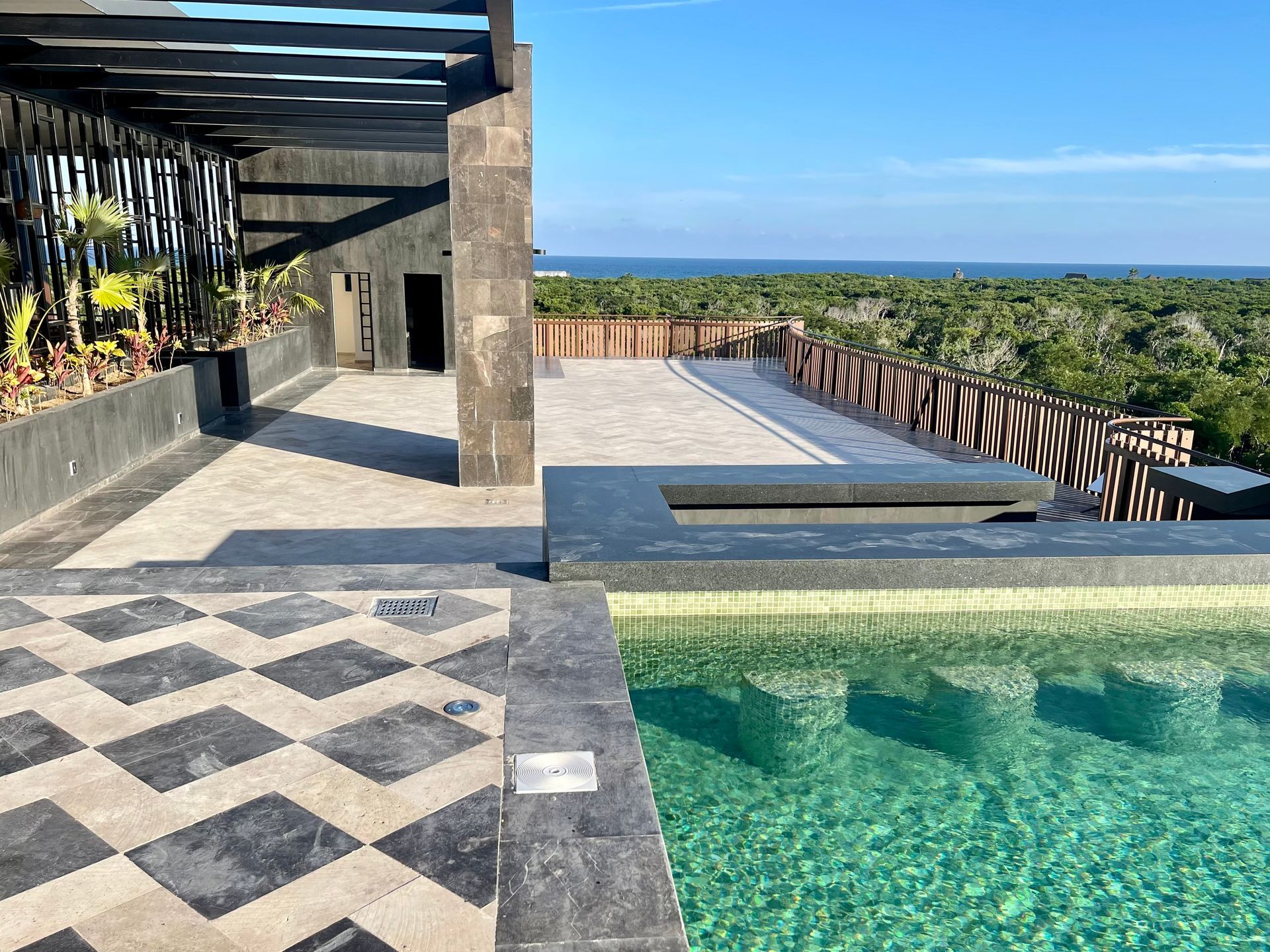 Rooftop pool with turquoise water, tiles, and a view of the ocean and trees.