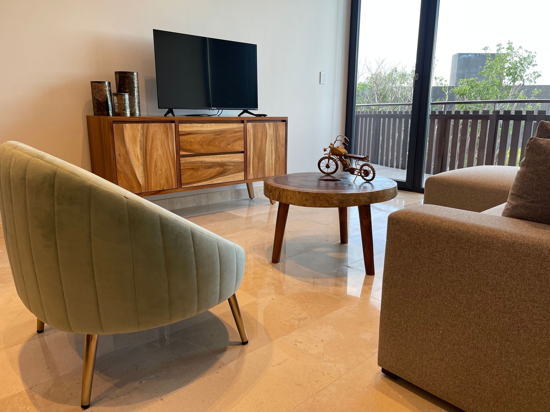 Sala de estar con muebles de madera: consola de TV, mesa de centro, silla y sofá. Grandes ventanales.