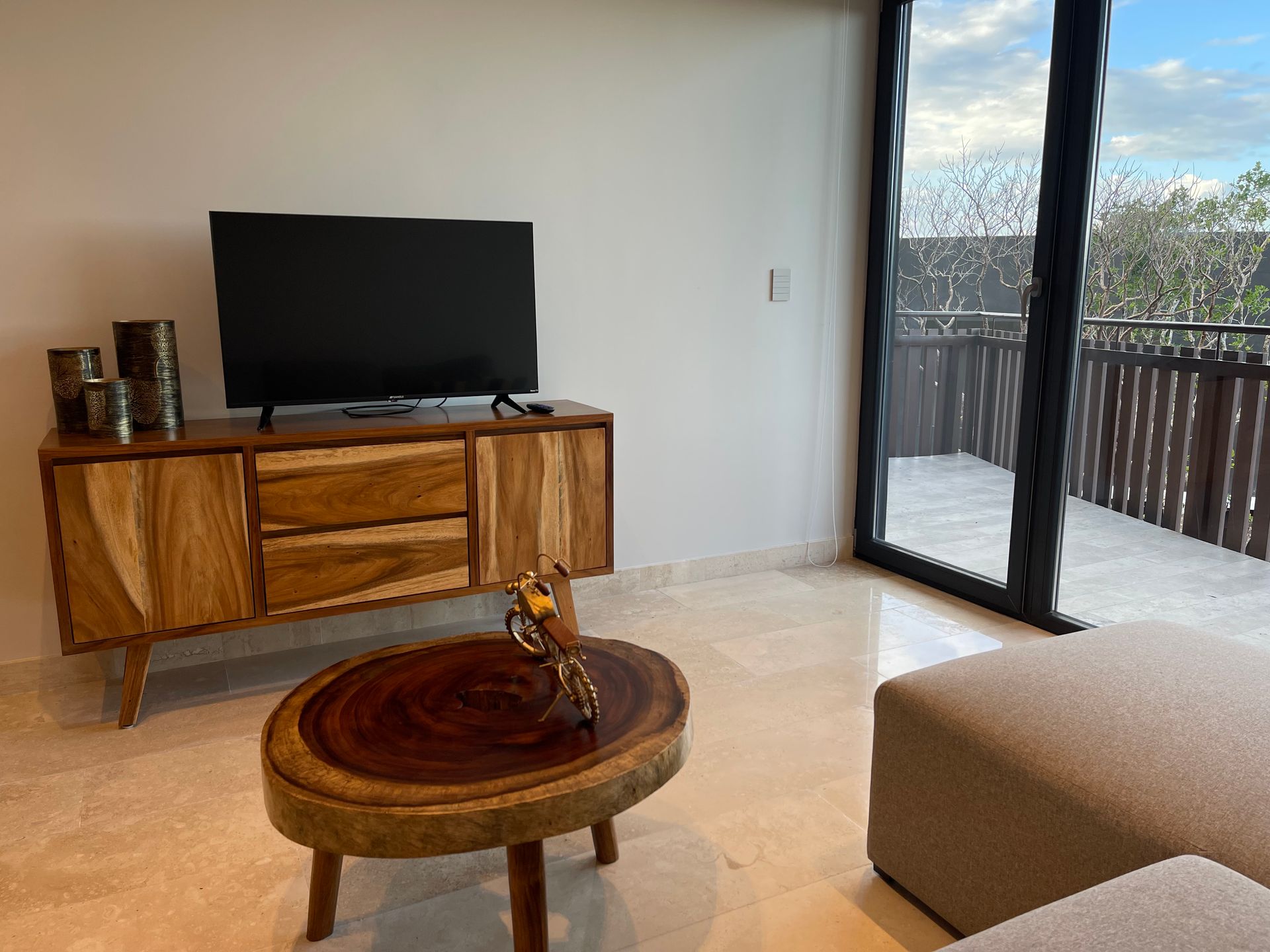 Sala con mueble de madera, TV, mesa de centro y vista al balcón.