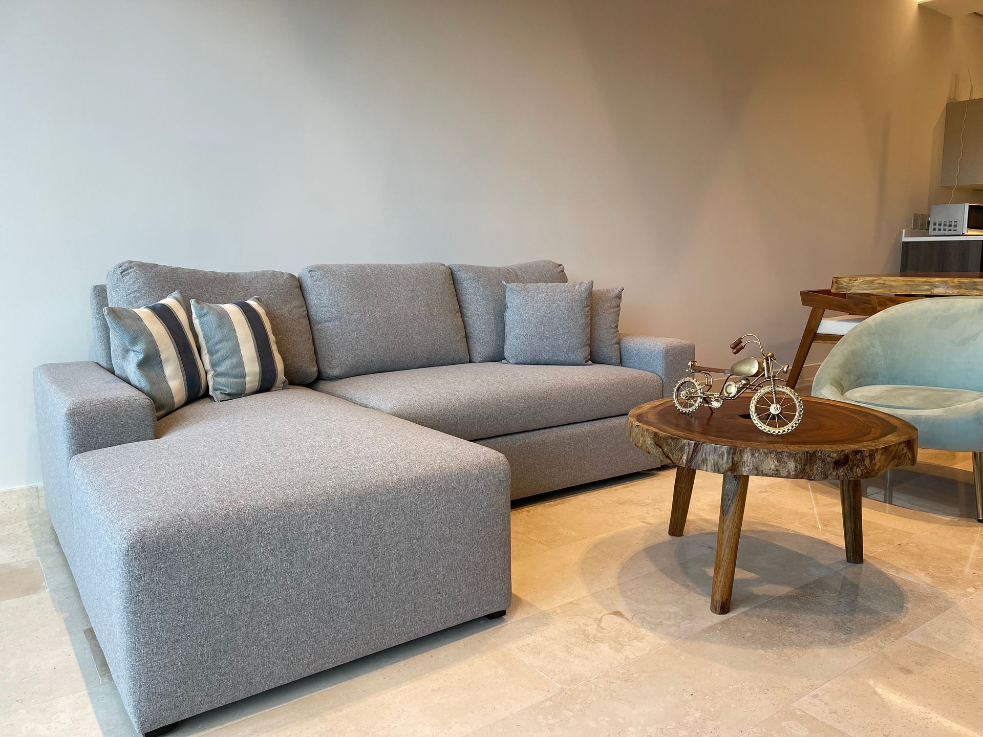 Sofá seccional gris con almohadas estampadas, mesa de café de madera y silla verde azulado en una sala de estar.