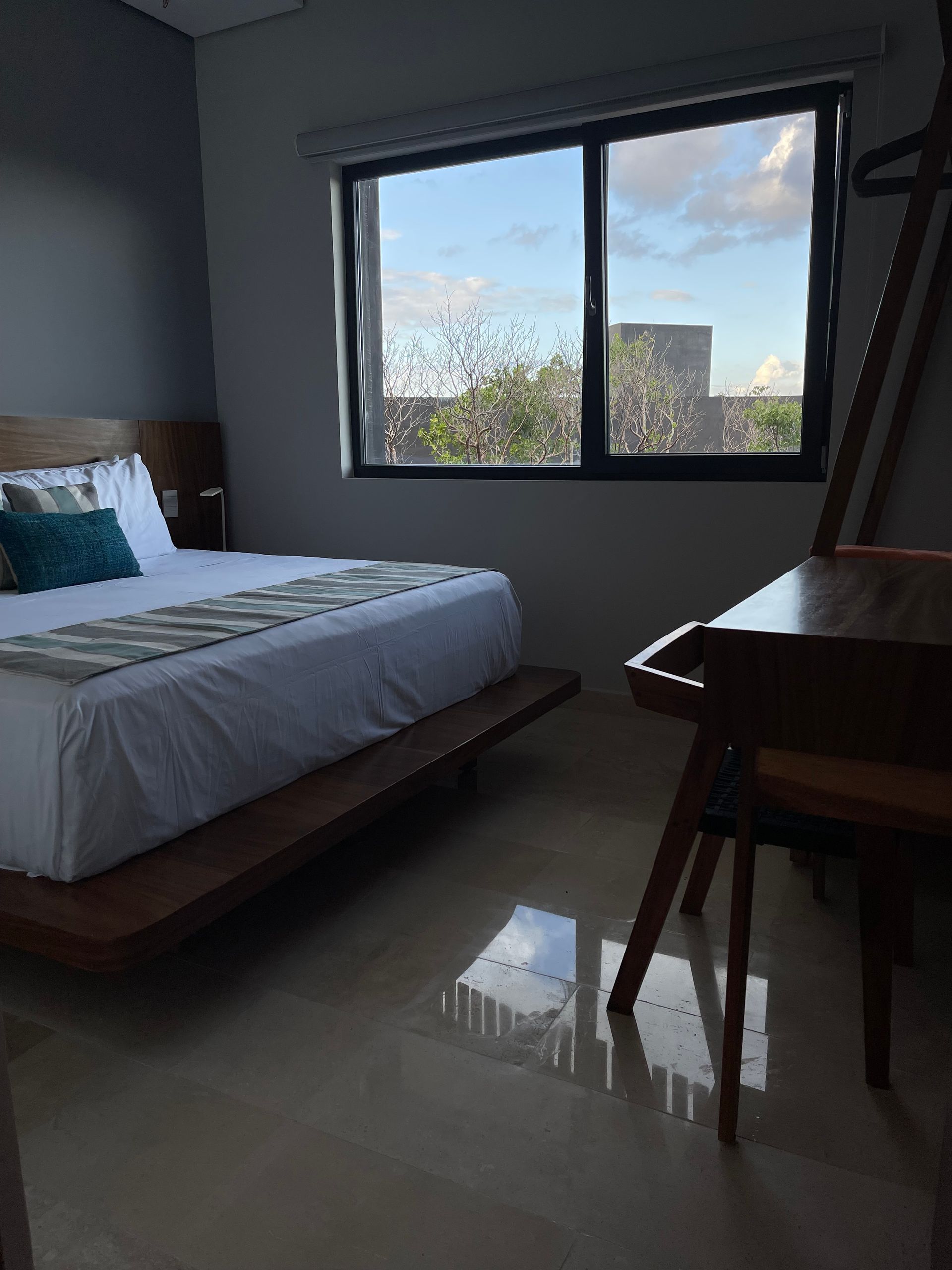 Dormitorio con cama, escritorio y ventana con vista al cielo y a los árboles.
