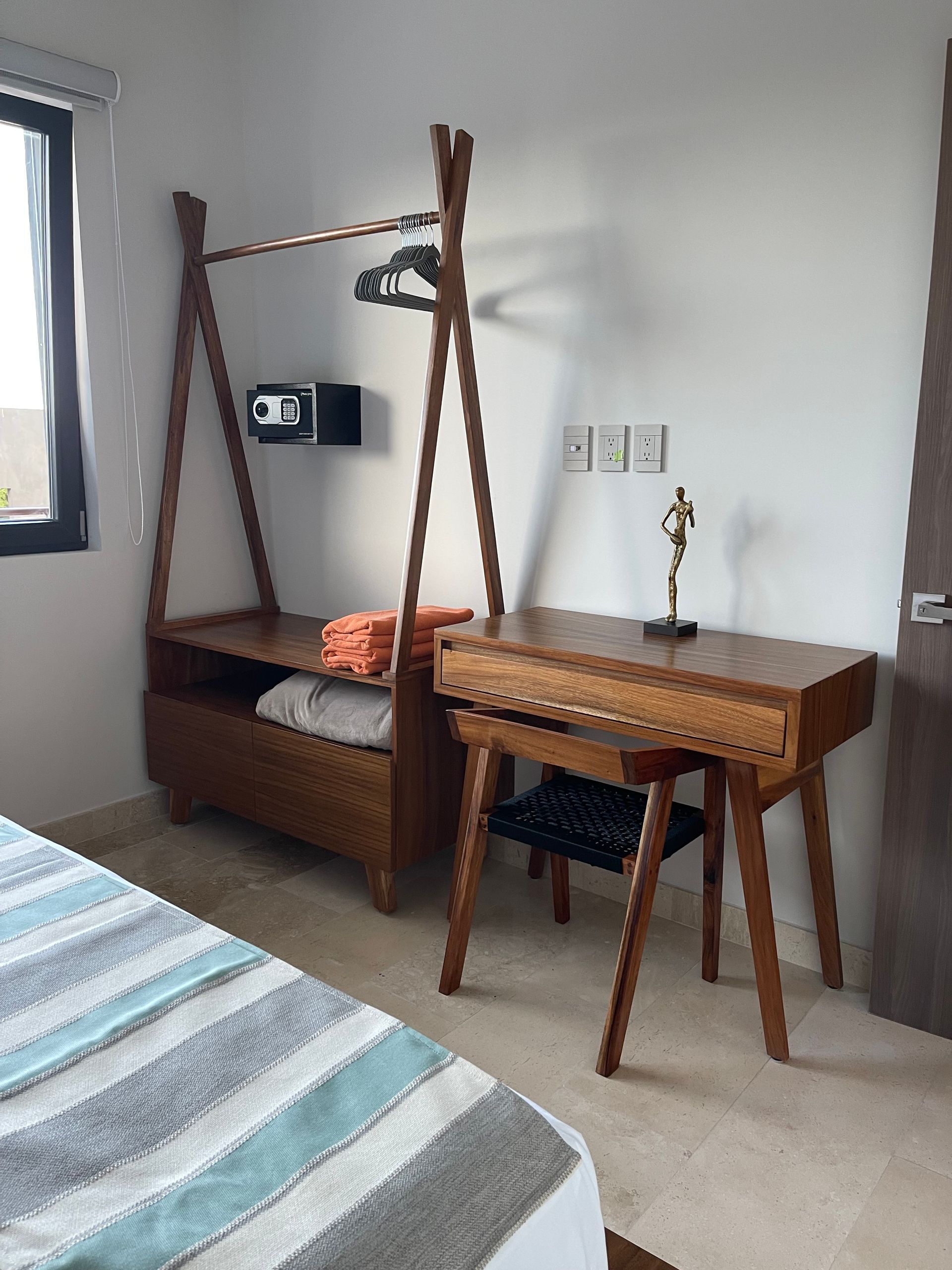 Armario de madera y escritorio en dormitorio con toallas y pequeña caja fuerte.