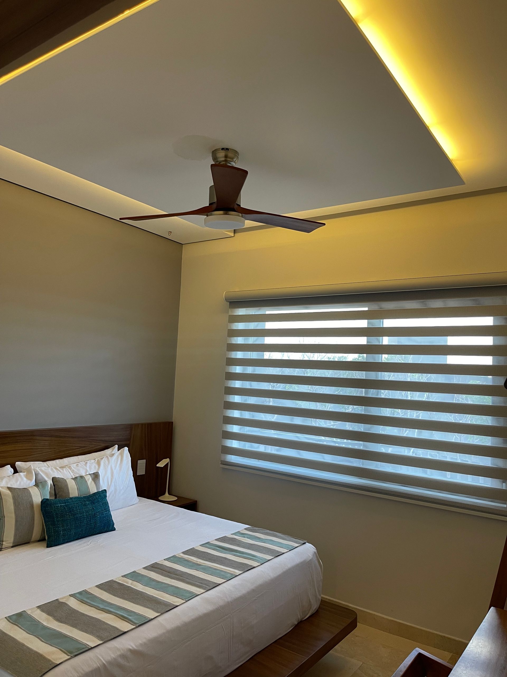 Dormitorio con cama, ventana, ventilador de techo e iluminación empotrada.