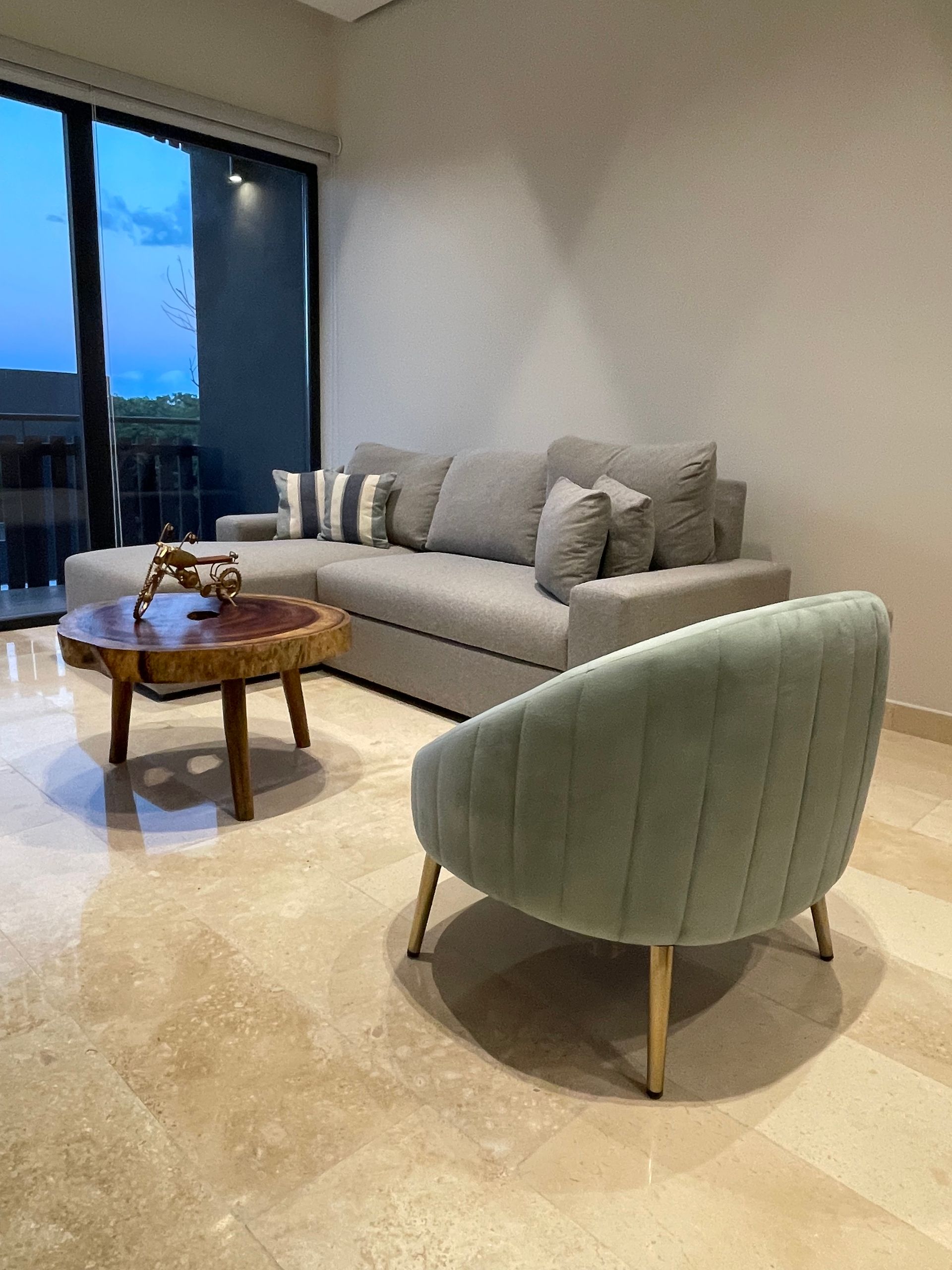Sala de estar con sofá seccional gris, sillón verde claro y mesa de centro de madera.