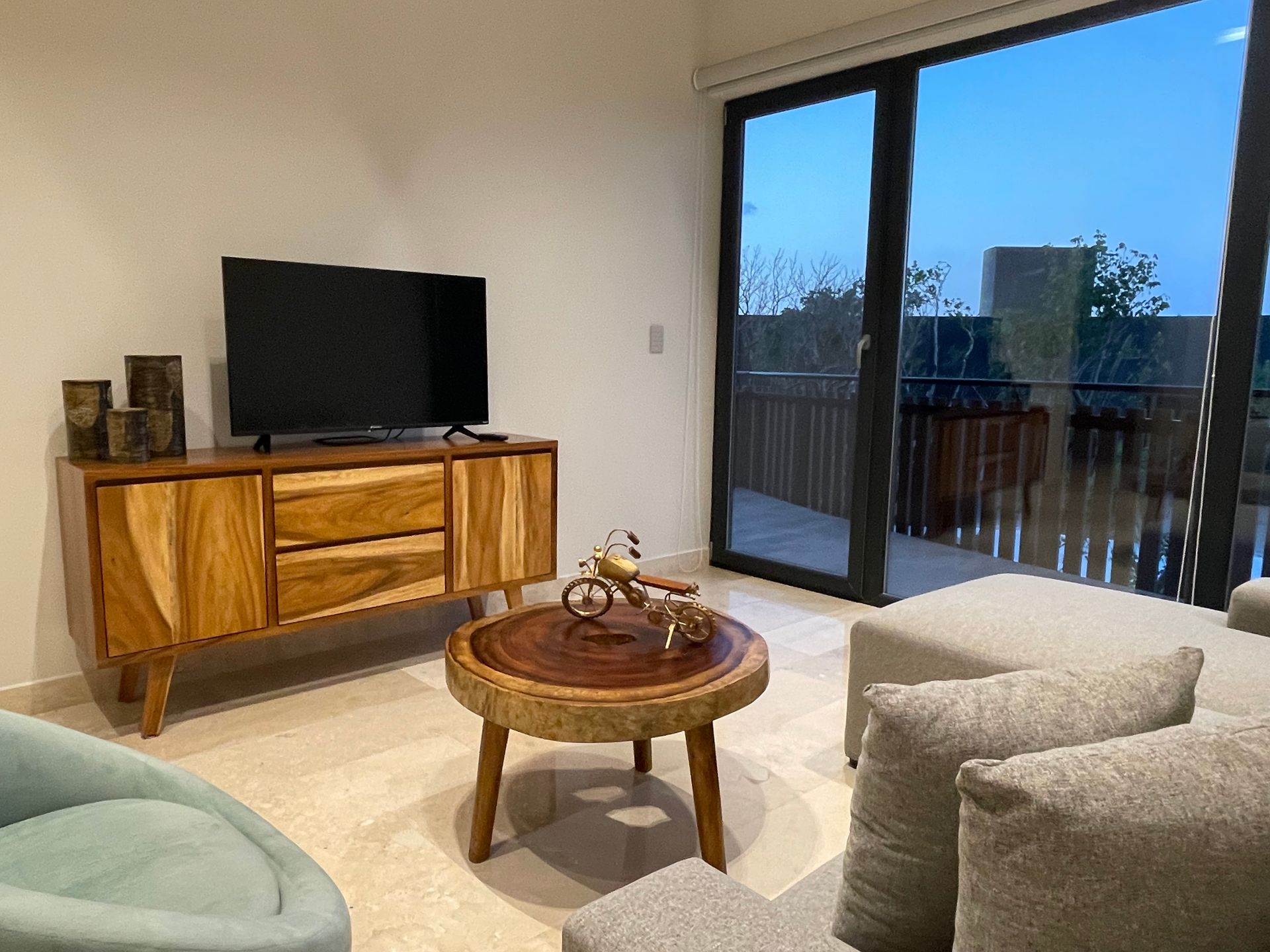 Sala de estar con TV, muebles de madera y vista a un balcón.