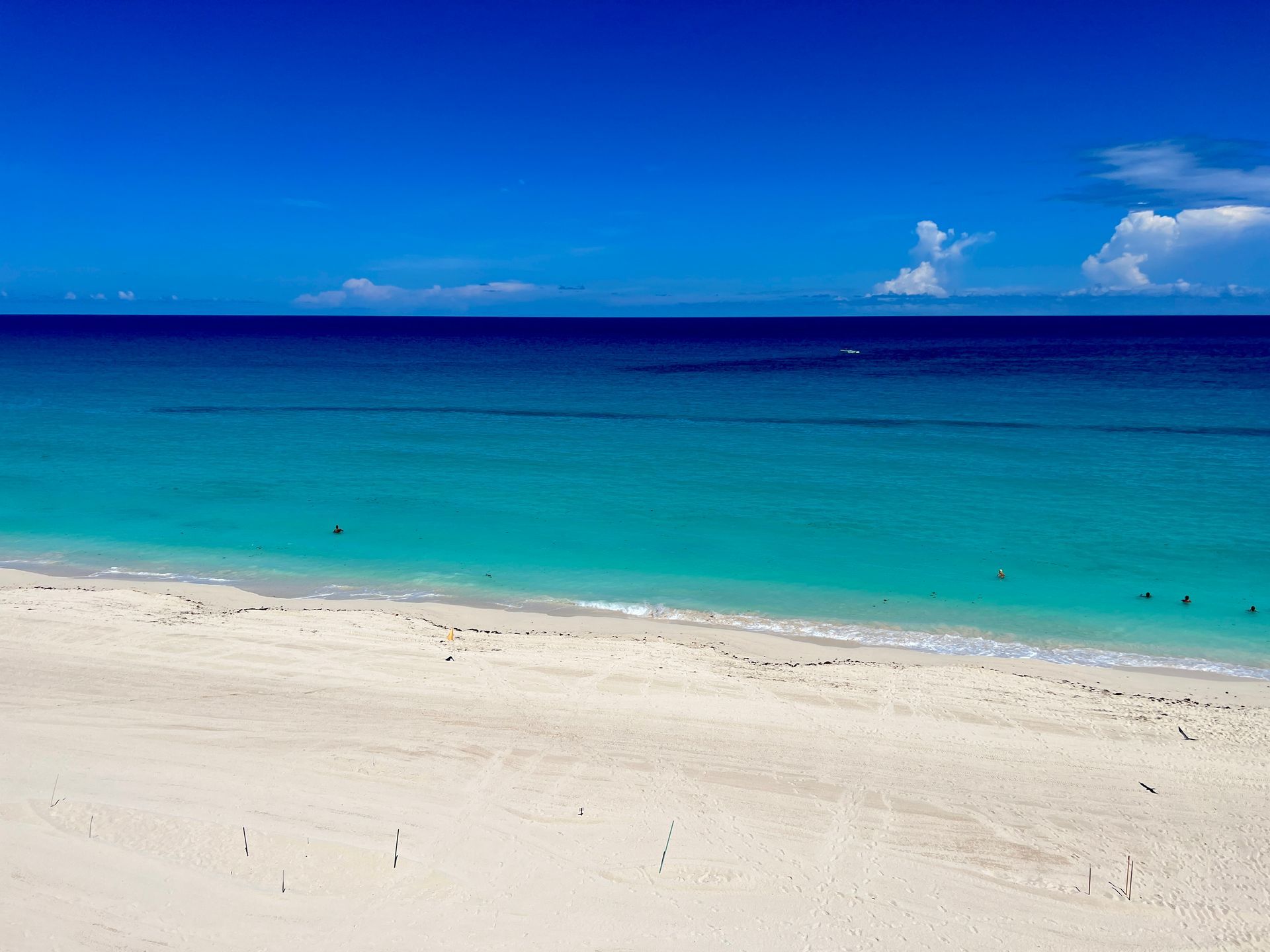 Vibrant blue ocean meets white sand beach under a clear, bright blue sky.