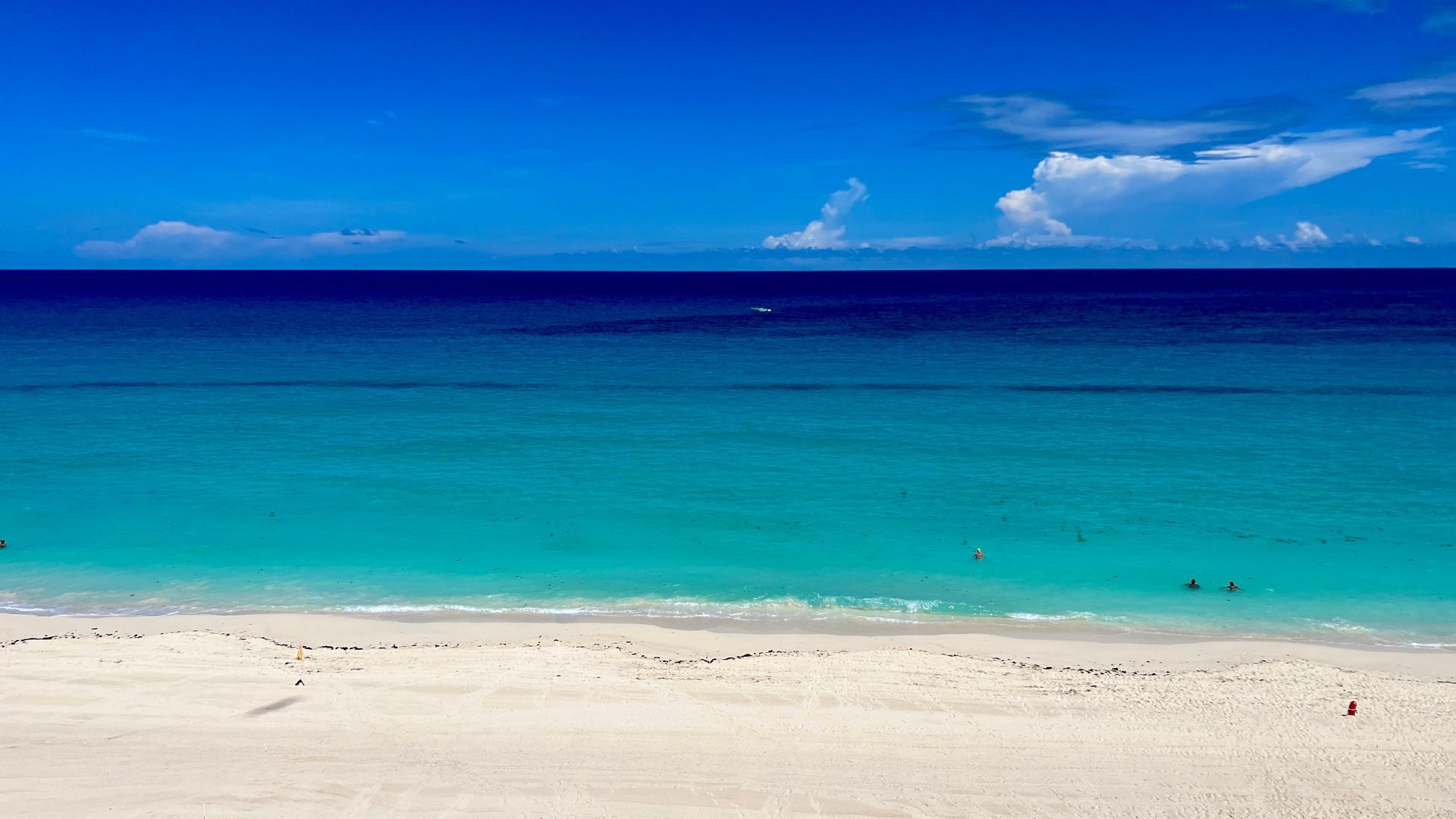 Bright blue sky over turquoise ocean, white sandy beach.