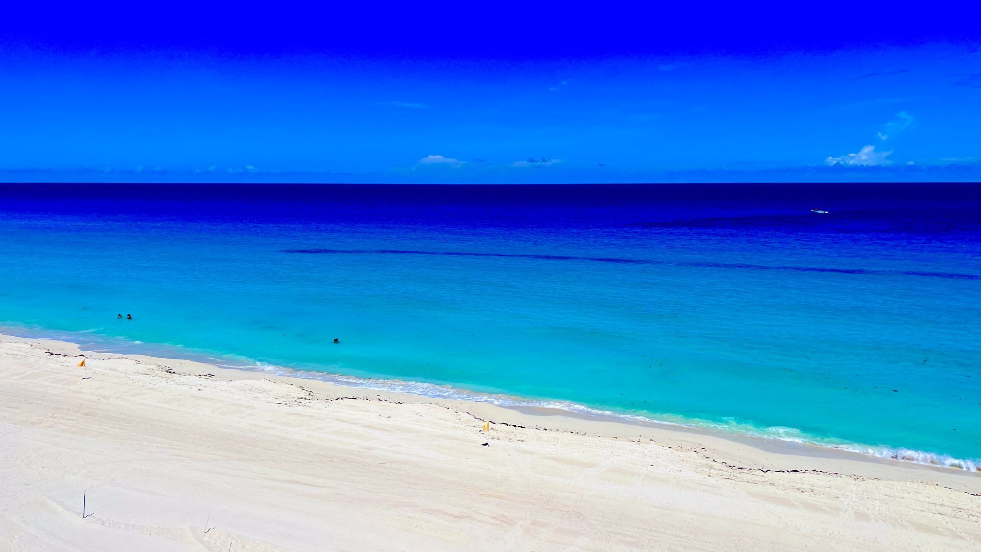 Un océano azul brillante se encuentra con una playa de arena blanca bajo un cielo azul claro.