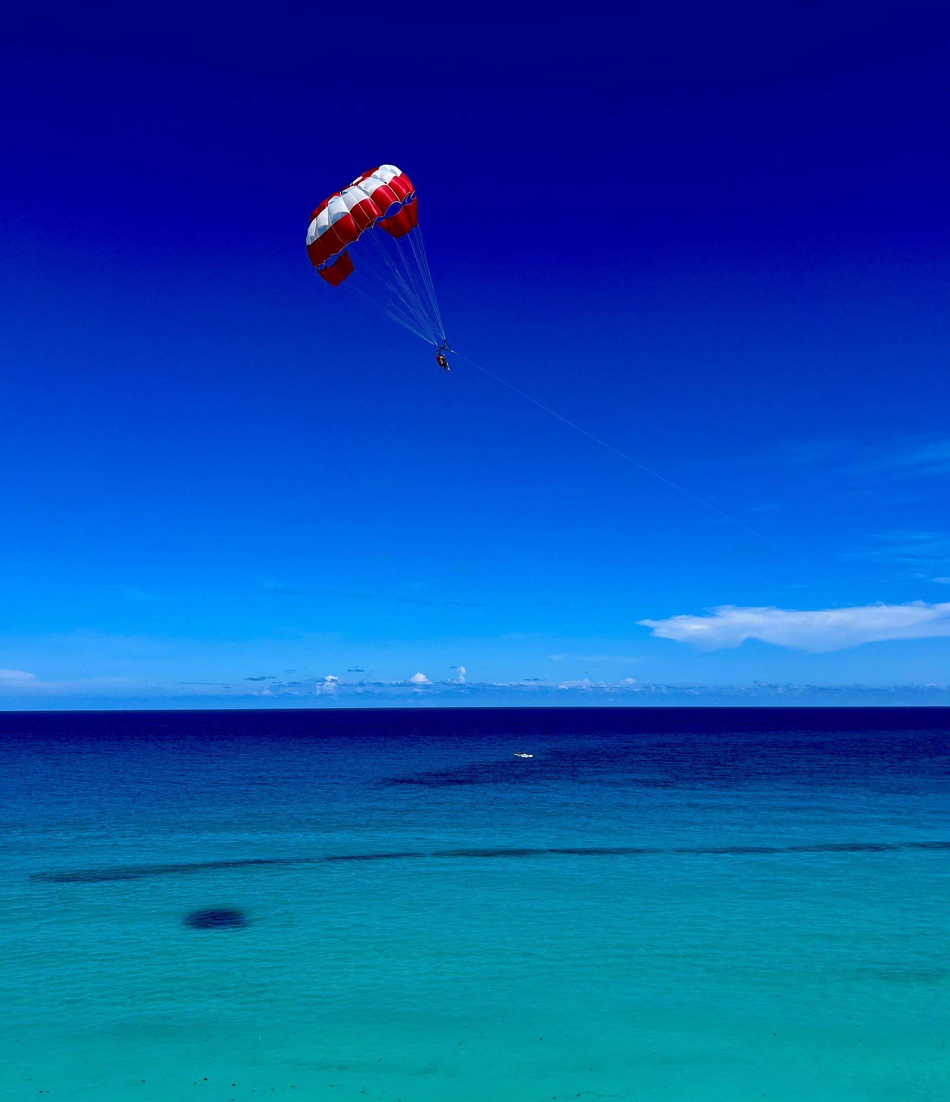 Parasailer over turquoise ocean under a bright blue sky.