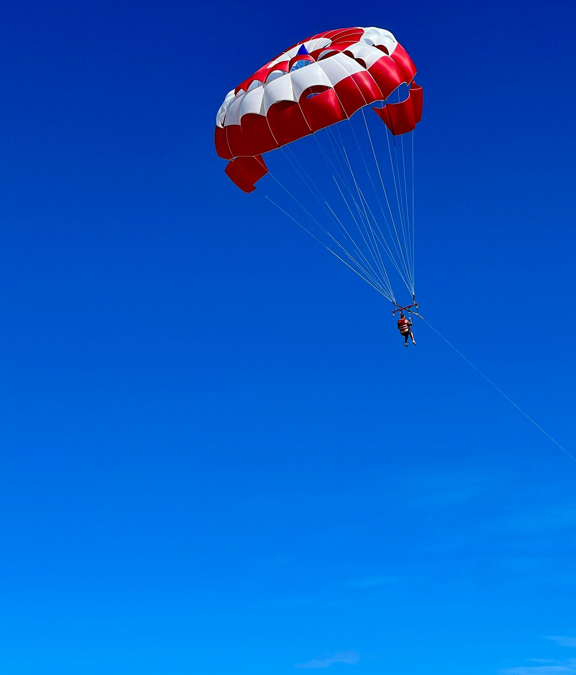 Parasailer in the bright blue sky, red and white canopy overhead.