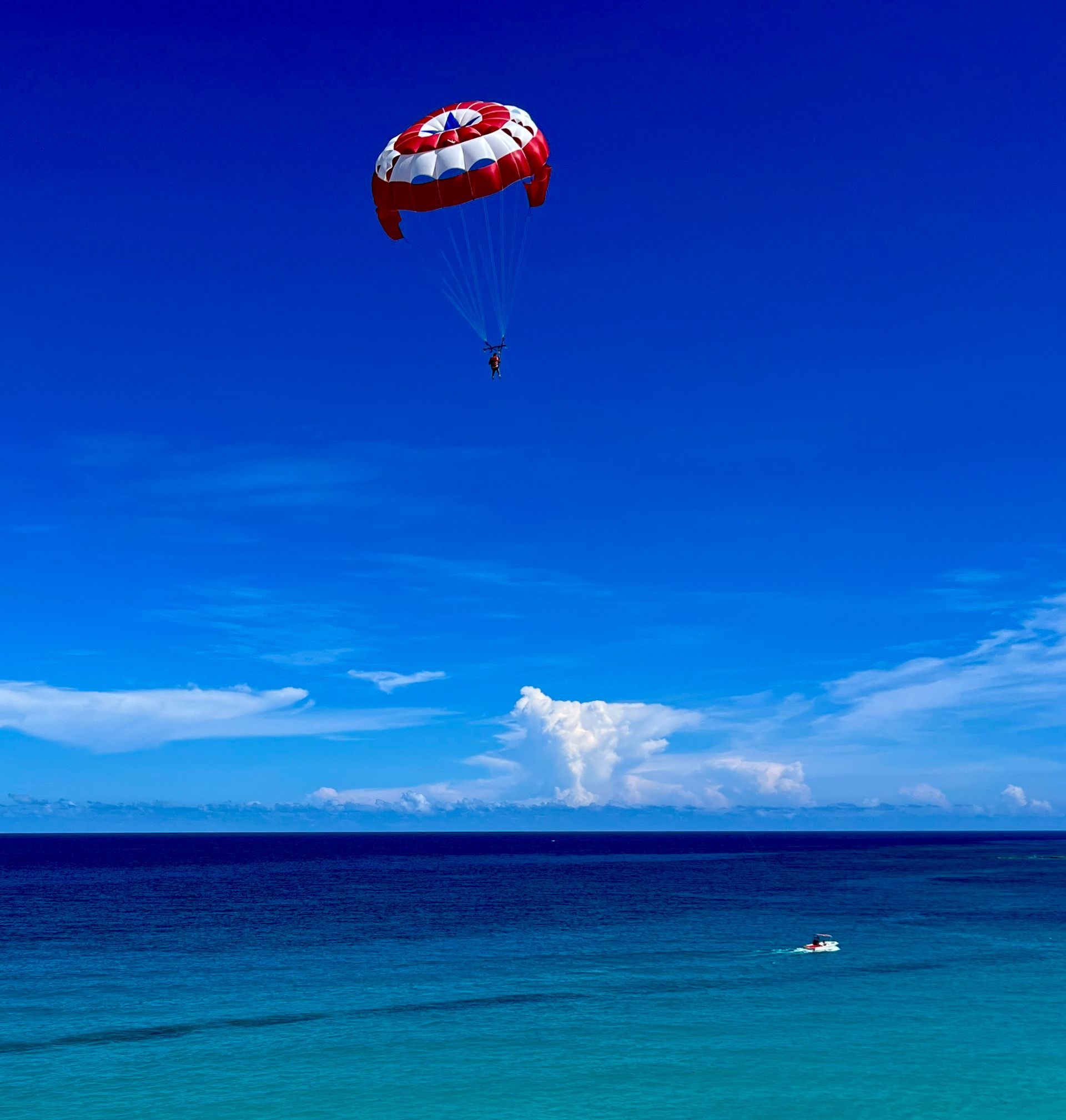 Parasailing over blue ocean under a bright blue sky with a boat below.