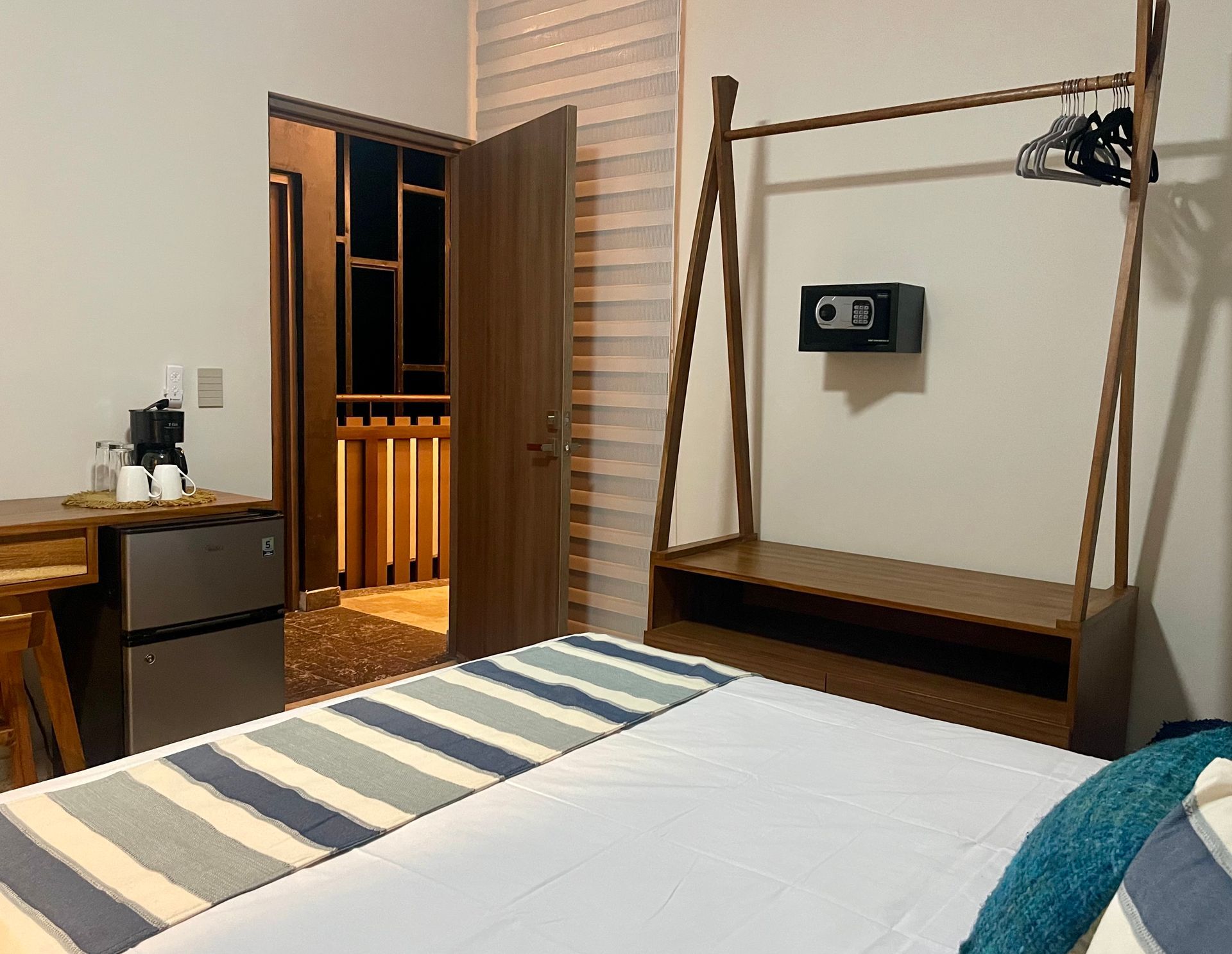 Interior del dormitorio: cama, puerta abierta al balcón, perchero de madera, caja fuerte, mininevera, escritorio .