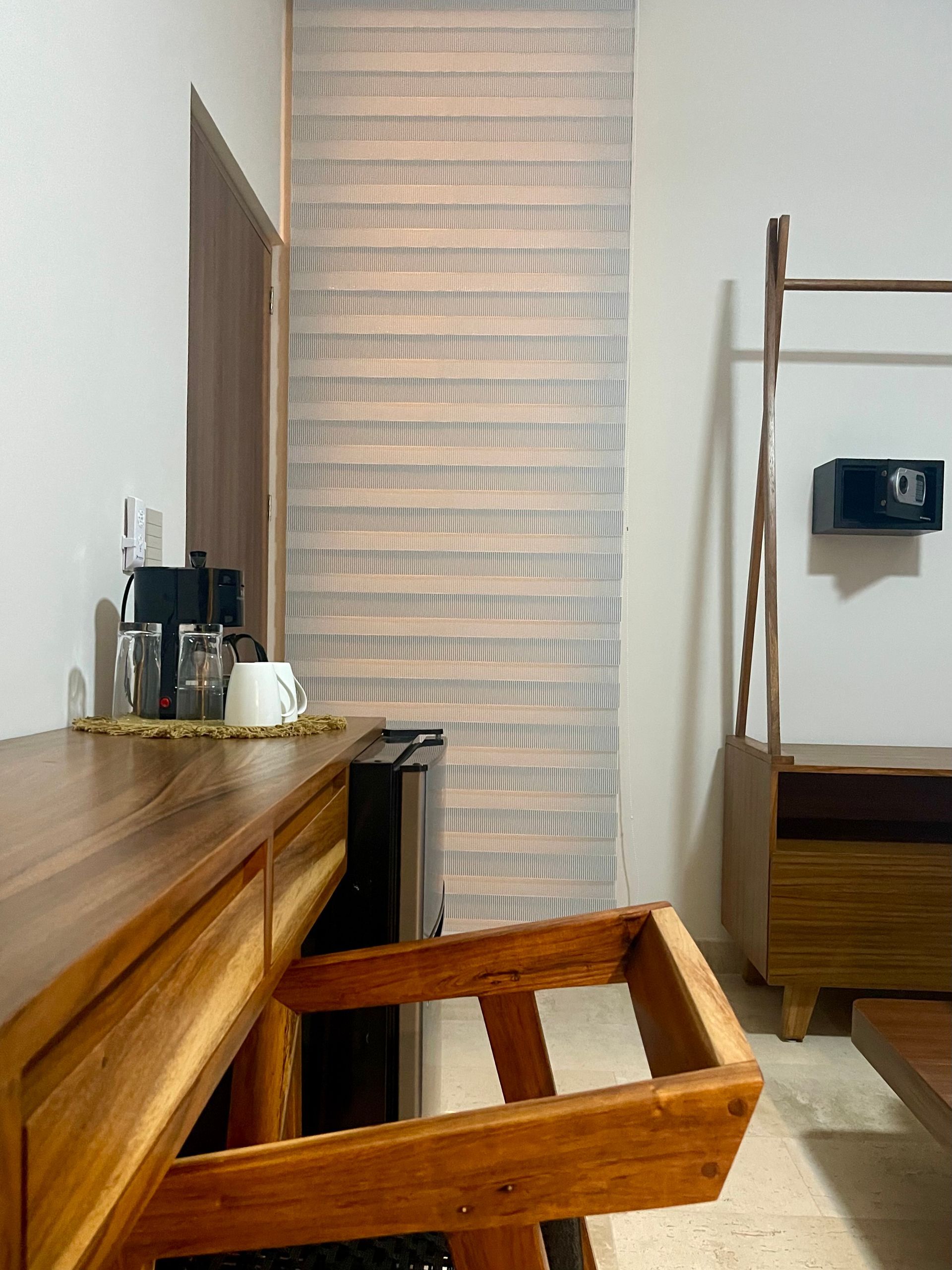 Mobiliario de habitación de hotel de madera, que incluye un escritorio con cafetera, silla y armario con caja fuerte.
