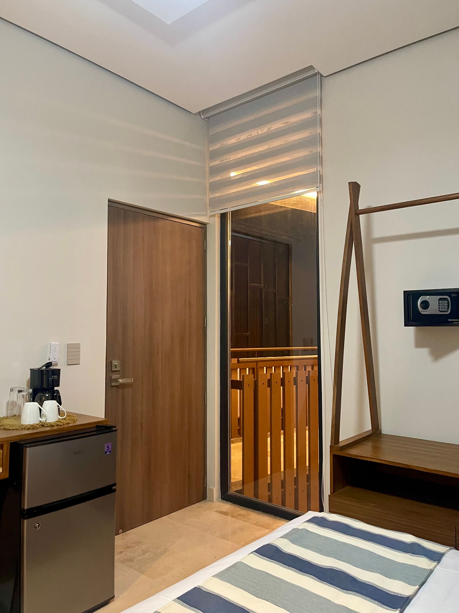 Dormitorio con mininevera, puerta, balcón, perchero y caja fuerte. Cubrecama azul y blanco.