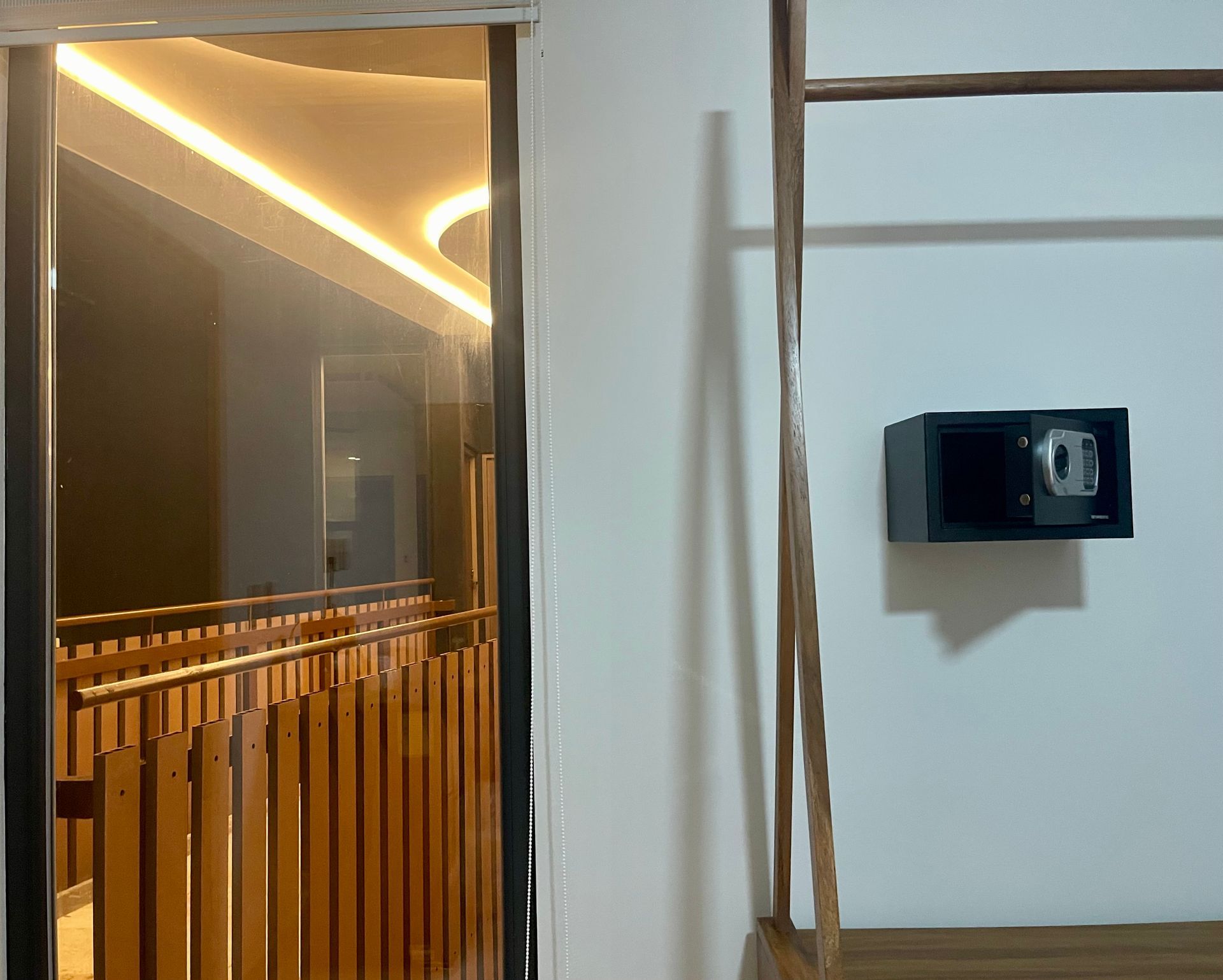 Vista interior de un edificio. Una caja fuerte negra está montada en una pared blanca junto a una escalera de madera.
