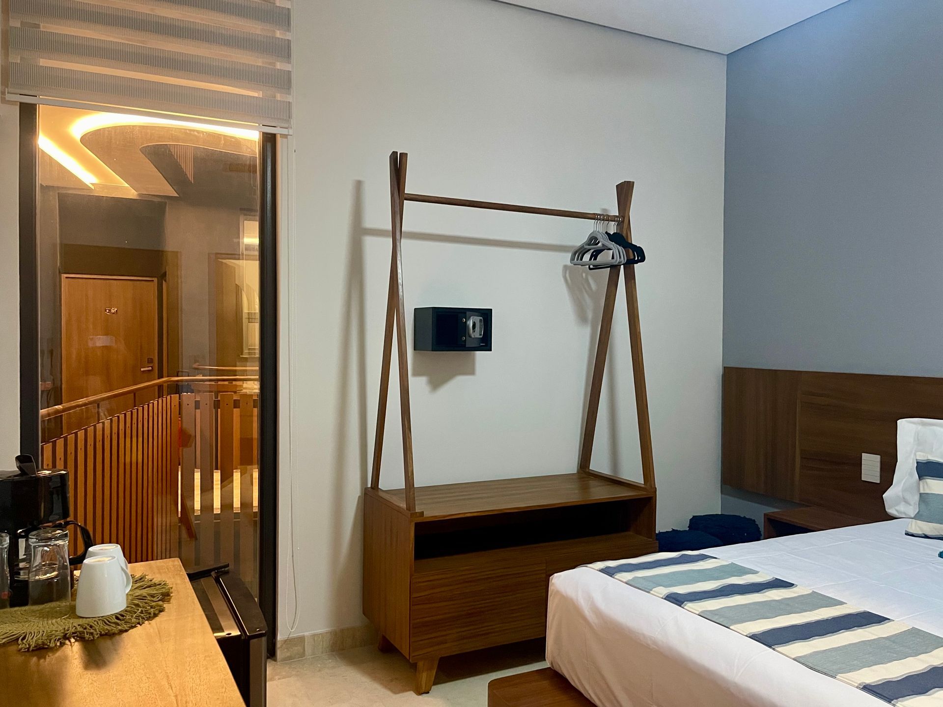 Habitación de hotel con cama, armario y acceso a una escalera de madera. Una cafetera sobre un escritorio.