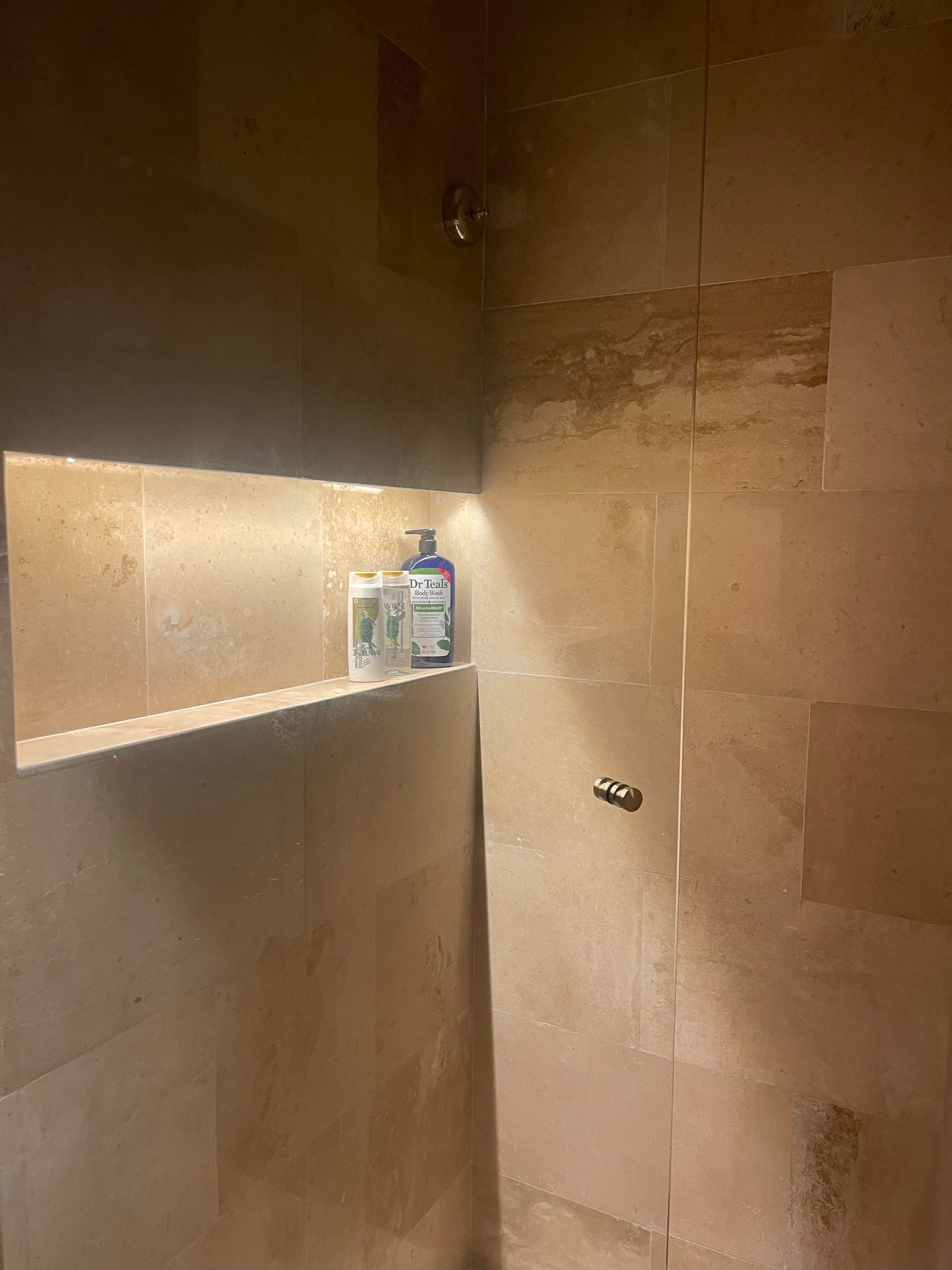 Ducha con repisa para jabón y champú. Paredes y cabezal de ducha con azulejos beige.