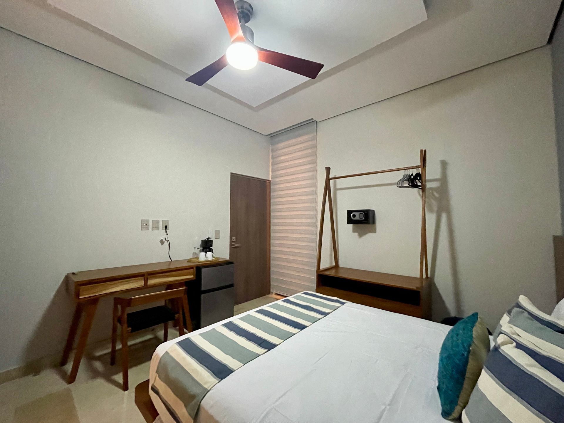 Dormitorio con cama, escritorio, cómoda, puerta y ventilador de techo.