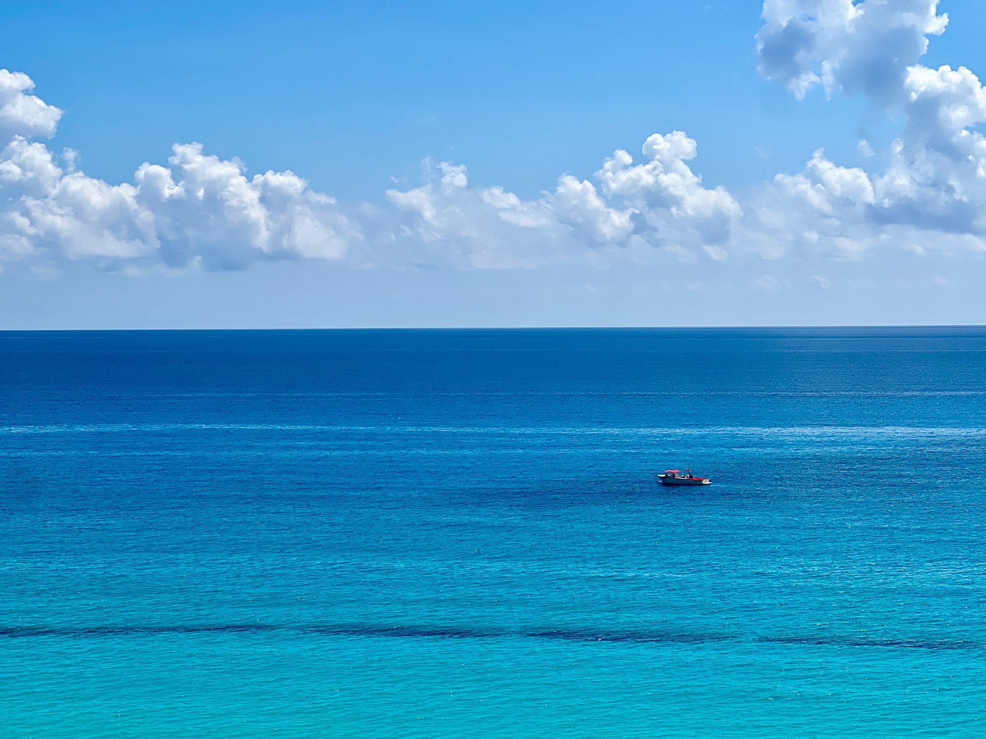 Vista al mar con un pequeño bote bajo un cielo azul con nubes hinchadas.