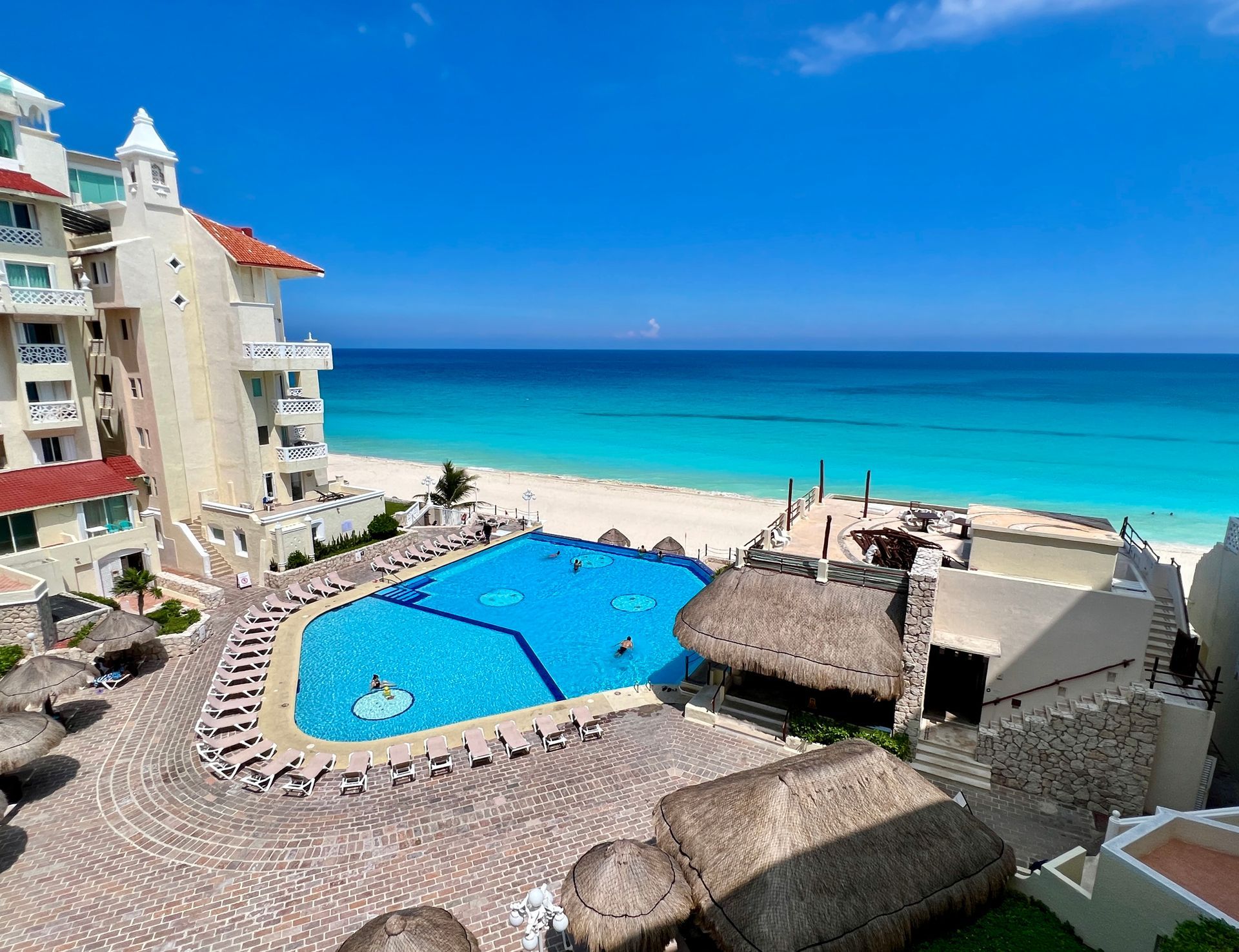 Resort frente al mar con agua turquesa, piscina y edificio blanco.
