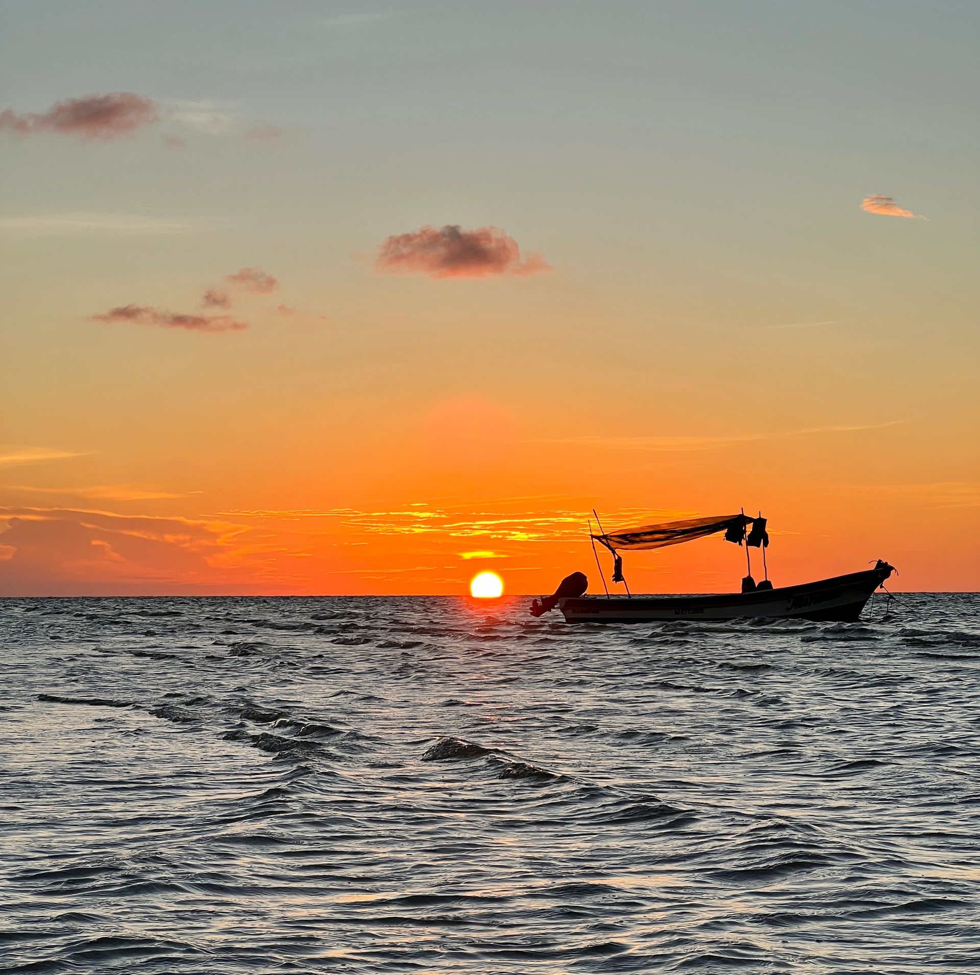Puesta de sol sobre el océano con un barco recortado contra el cielo naranja.