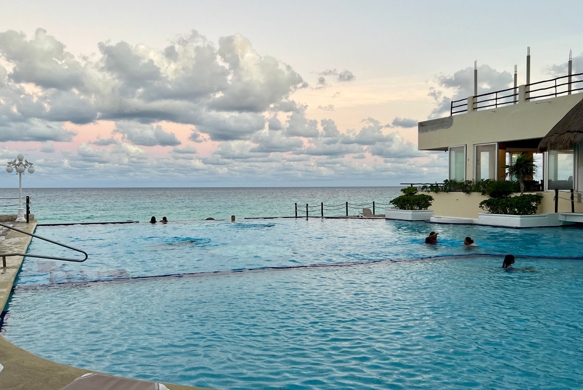 Piscina con vista al mar, gente nadando, cielo nublado.