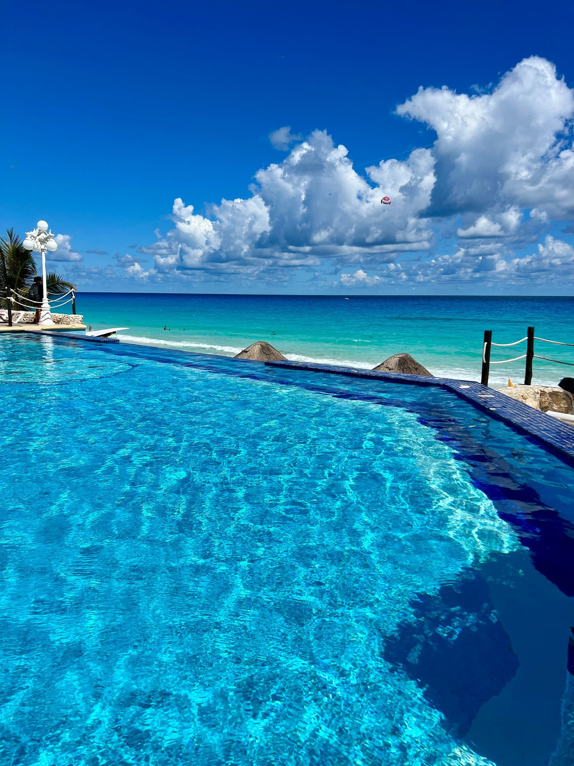 Piscina infinita con vista al océano turquesa bajo un cielo azul con nubes.