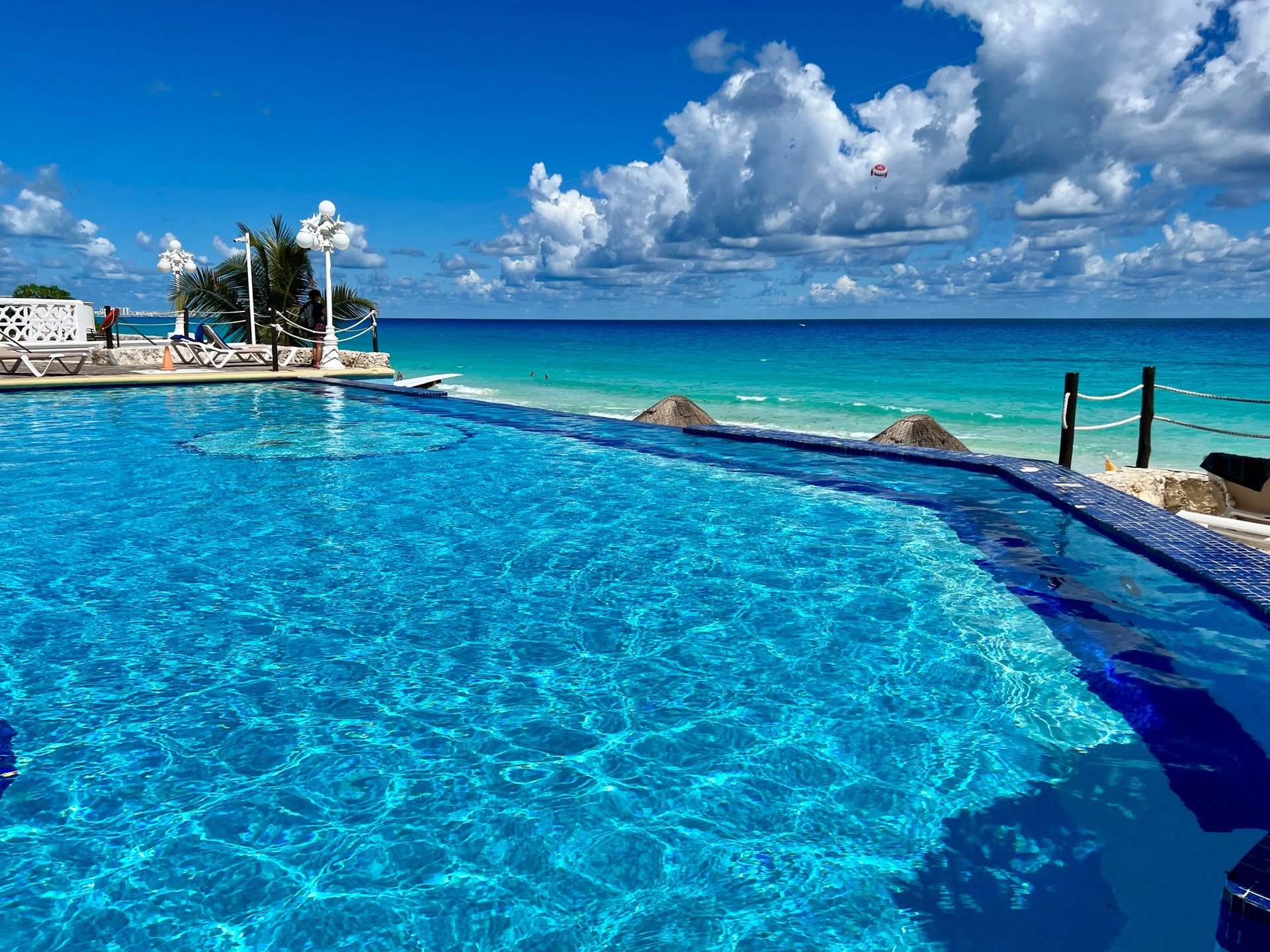 Infinity pool overlooking a turquoise ocean under a bright blue sky with fluffy clouds.