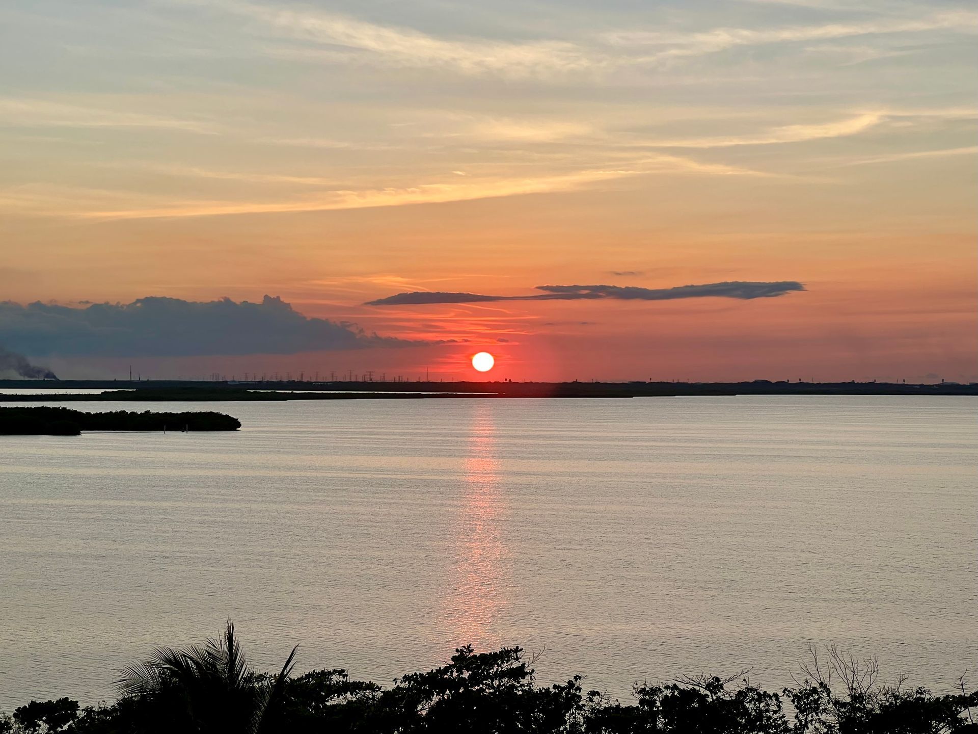 Puesta de sol sobre aguas tranquilas, reflejando luz naranja y roja, con un horizonte recortado.