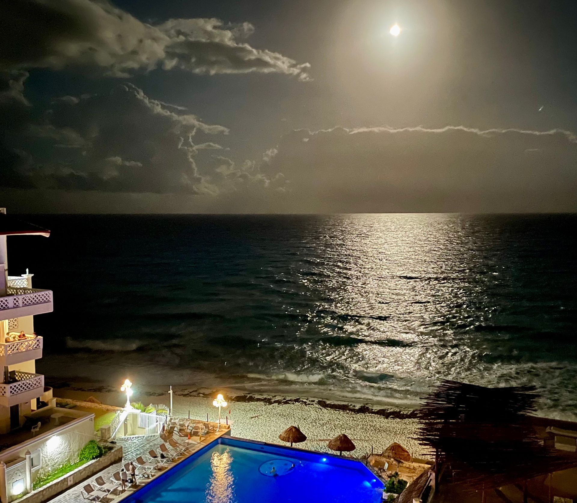 Moonlit ocean view with a pool and buildings; light reflecting on the water.