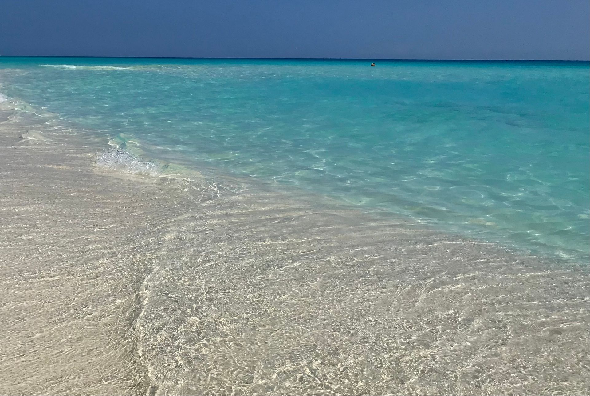 El agua turquesa brillante baña una playa de arena blanca bajo un cielo azul claro.