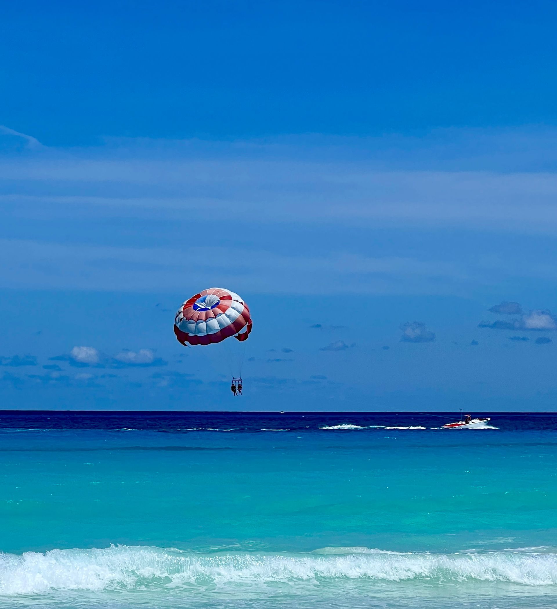 Parasailing sobrevolando el océano turquesa bajo un cielo azul, con un barco visible.