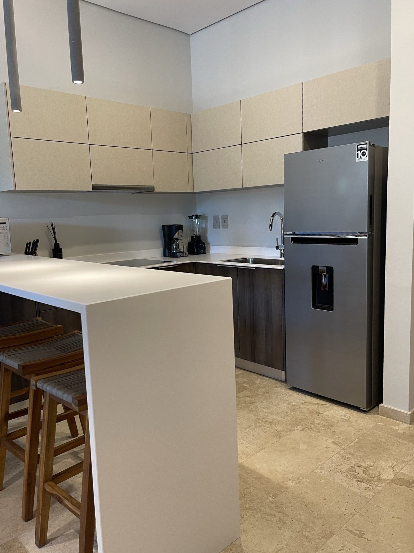 Cocina moderna con encimera blanca, gabinetes beige y refrigerador de acero inoxidable.