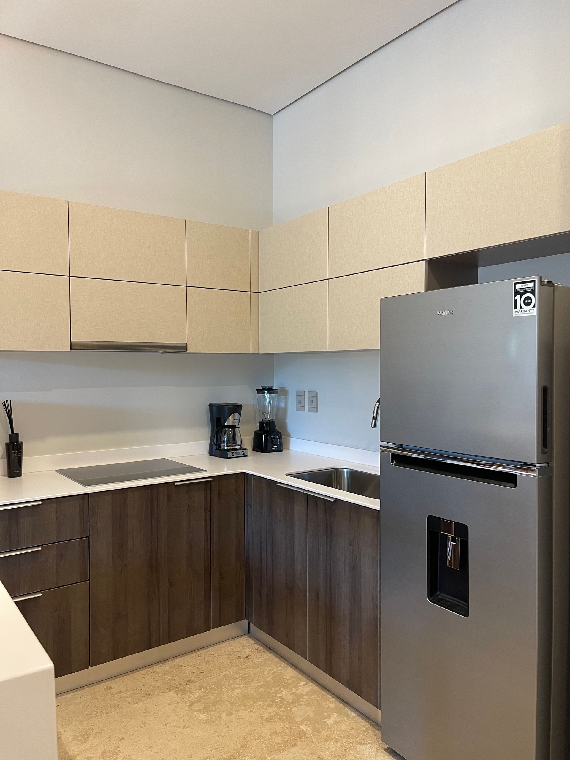 Cocina moderna con gabinetes superiores de color claro, gabinetes inferiores de madera oscura y refrigerador.