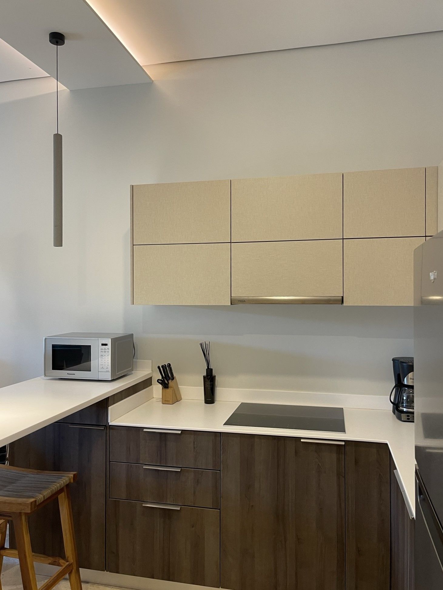 Cocina moderna con gabinetes de color beige claro, gabinetes inferiores  color marrón oscuro, encimeras blancas y microondas.