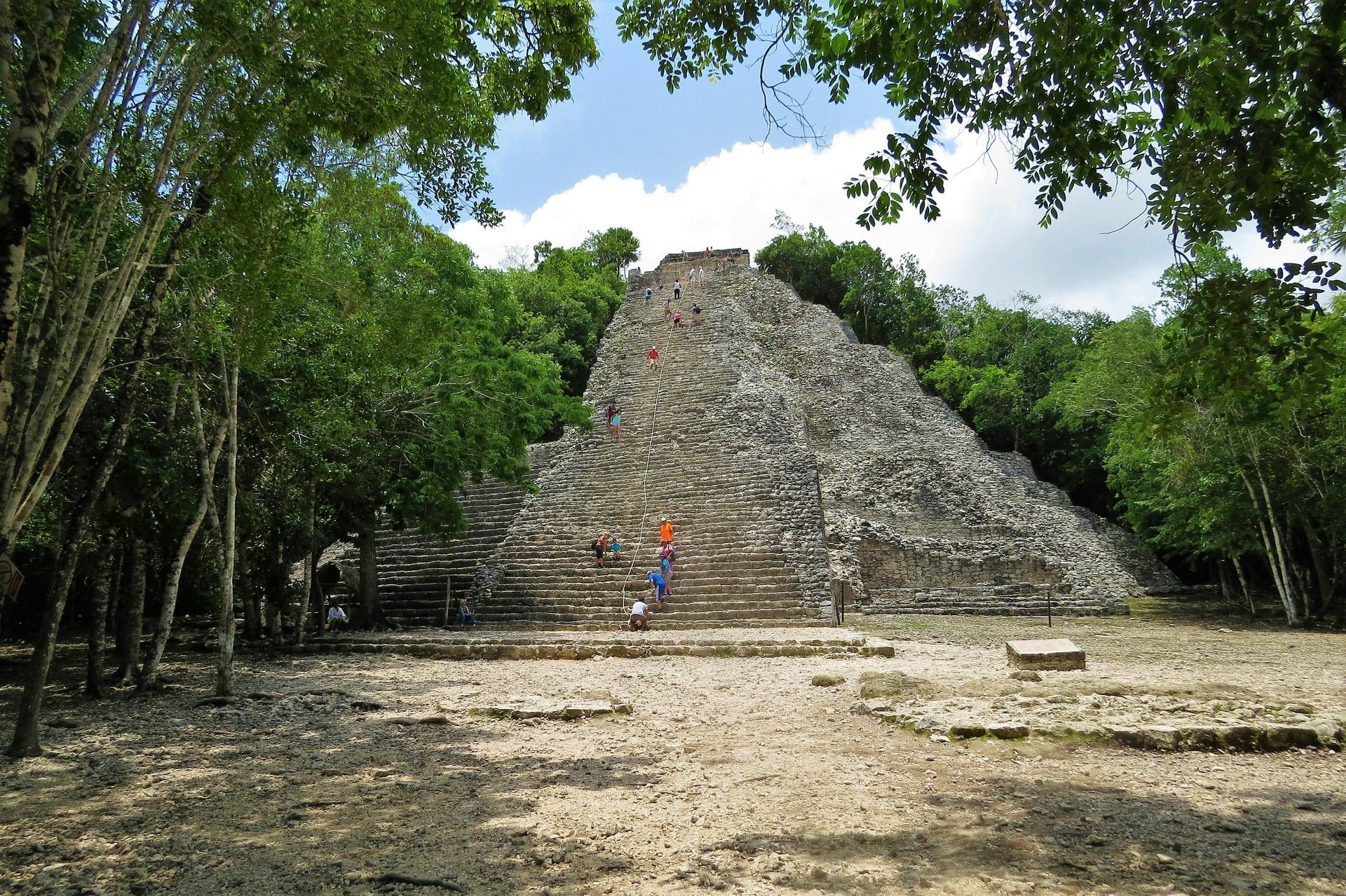 Pirámide de piedra en un entorno selvático; , rodeada de árboles y un cielo brillante.