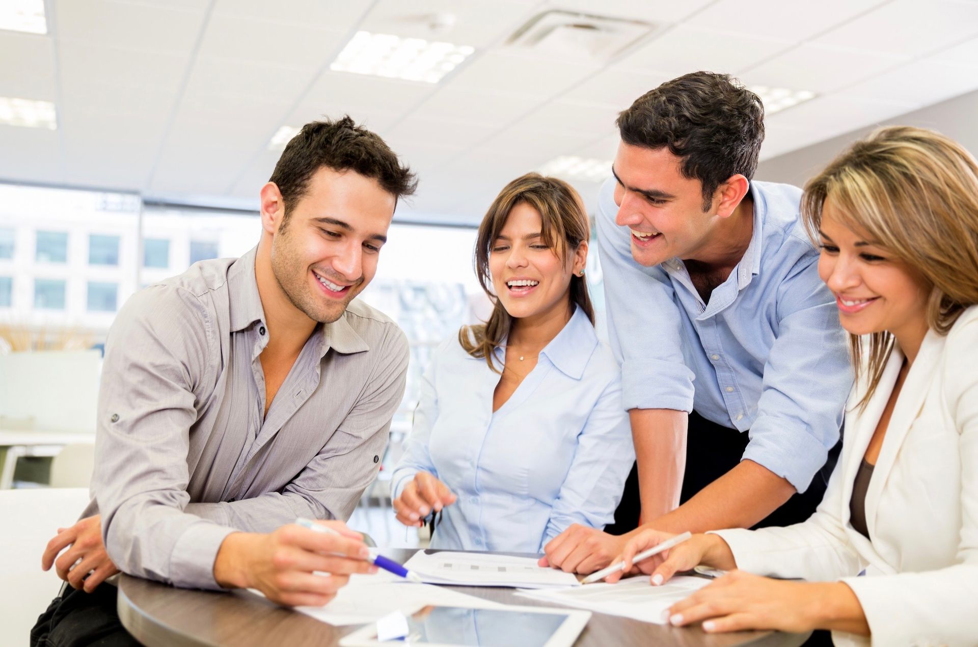 A group of people are sitting around a table looking at a tablet.