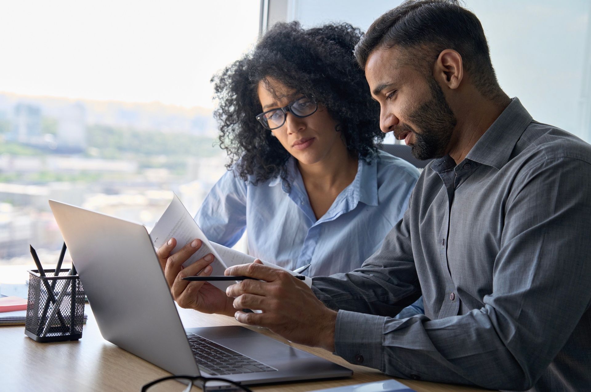 A man and a woman are sitting at a desk looking at a laptop.