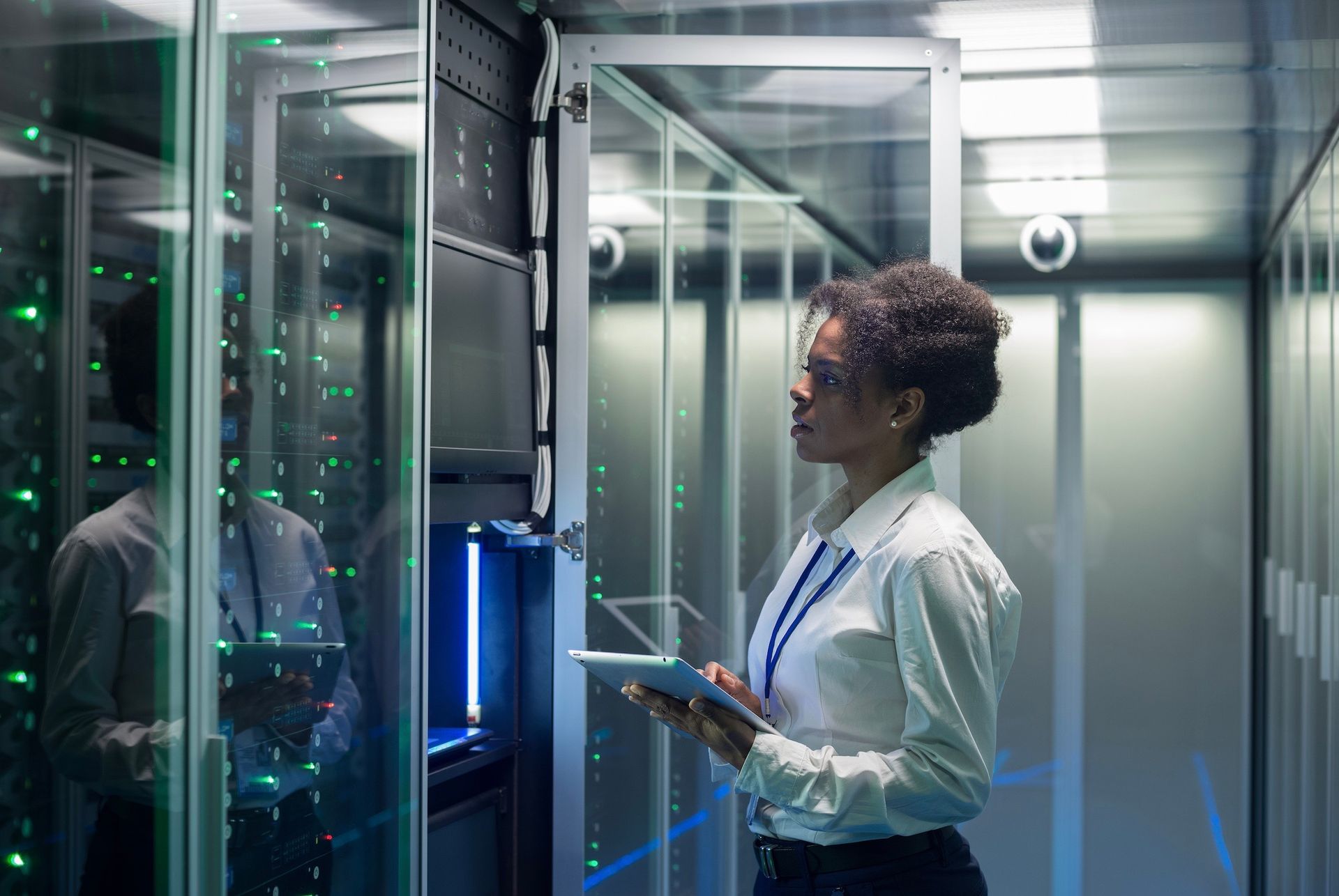 A woman is standing in a server room holding a tablet.