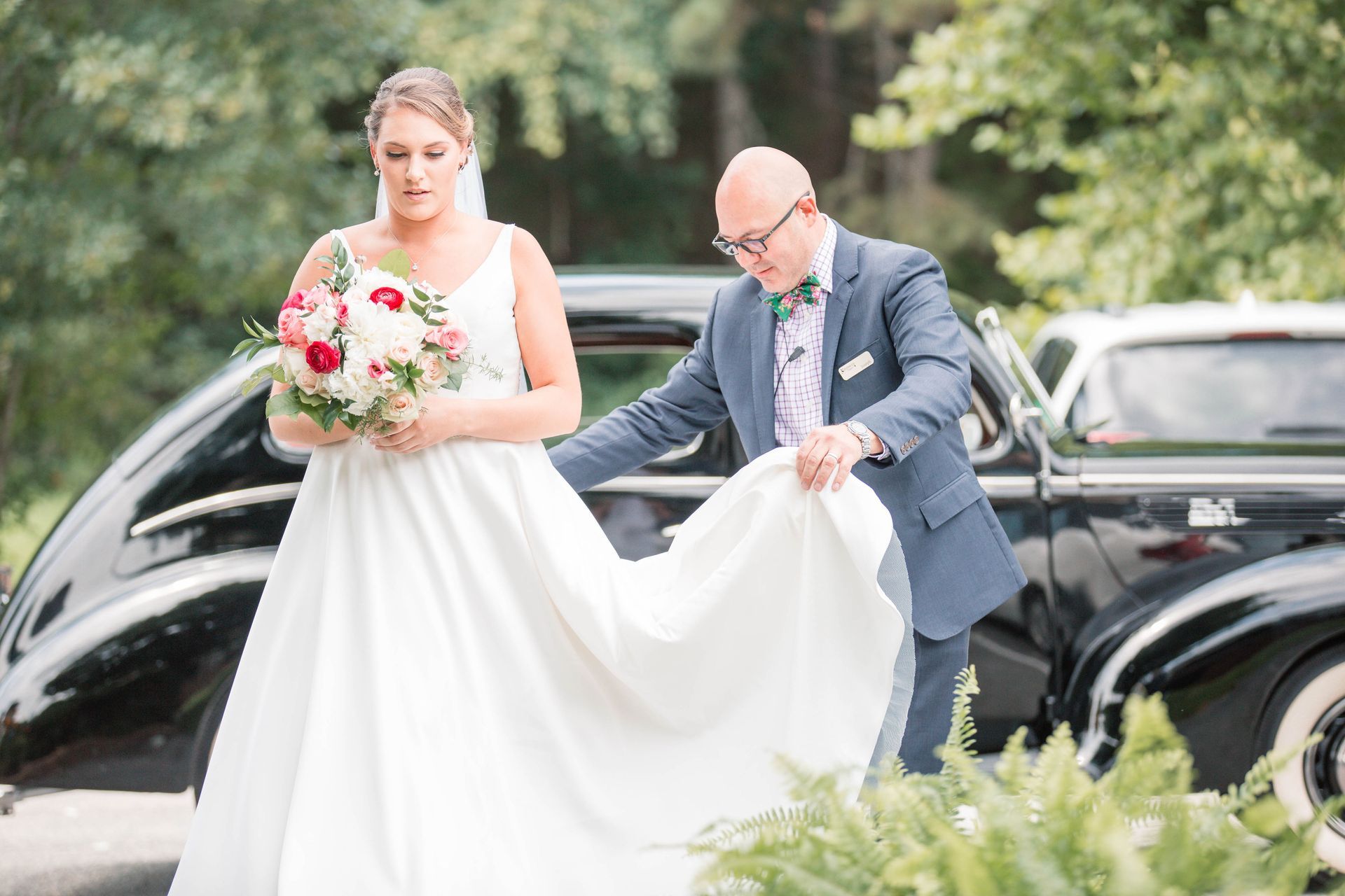 A bride and groom are standing in front of a black car.