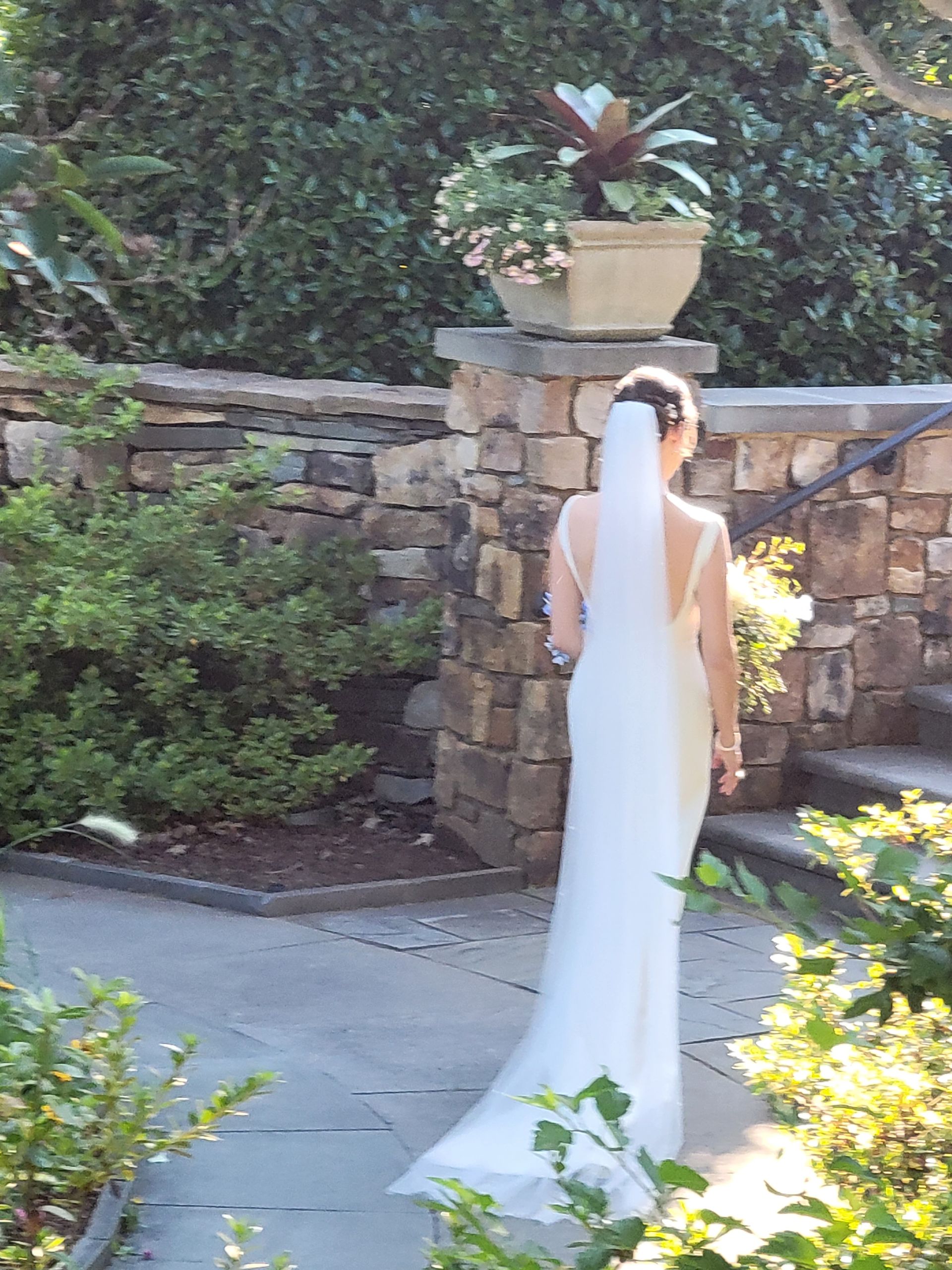 The bride is wearing a long veil and standing in front of a stone wall.