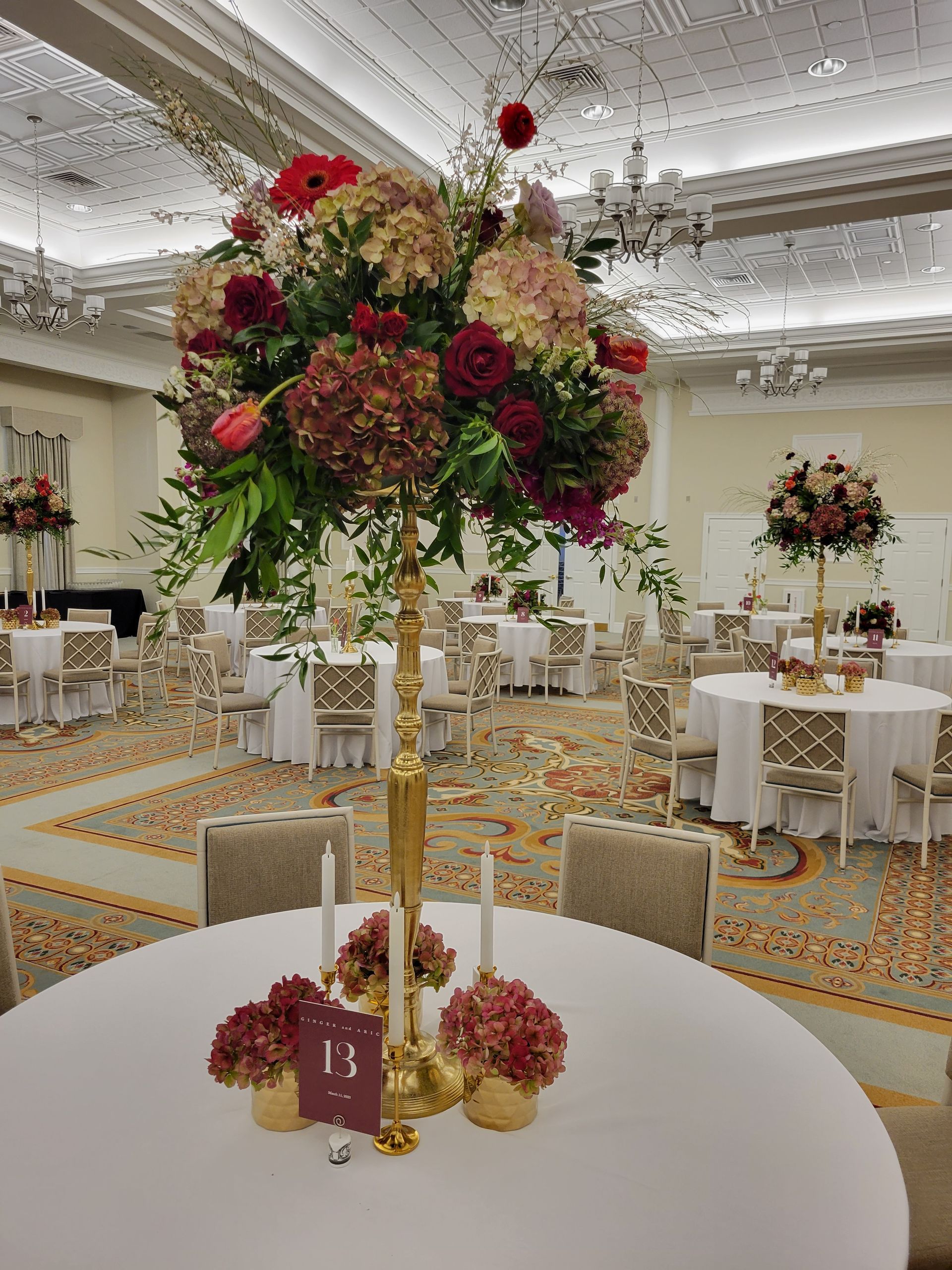 A table with a vase of flowers and candles on it in a large room.