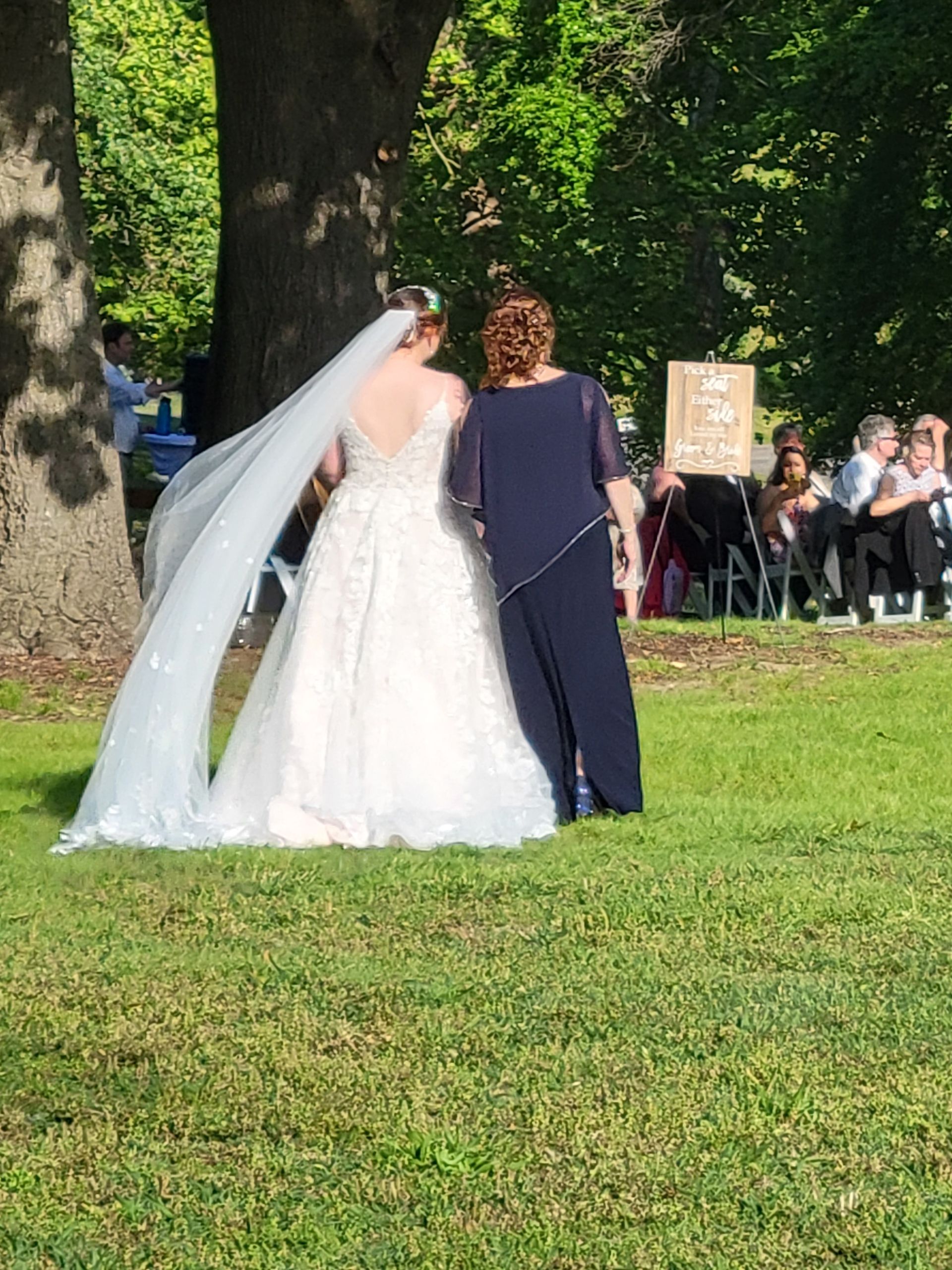 A bride and her mother are standing in a grassy field.